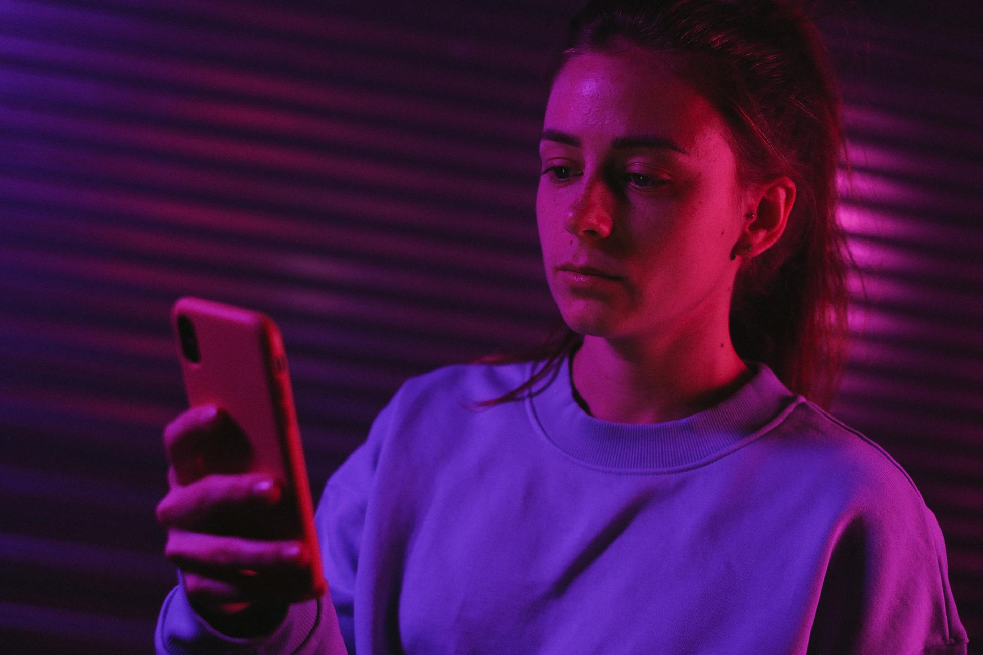 Une femme utilisant son téléphone dans une pièce sombre avec des lumières colorées | Source : Pexels