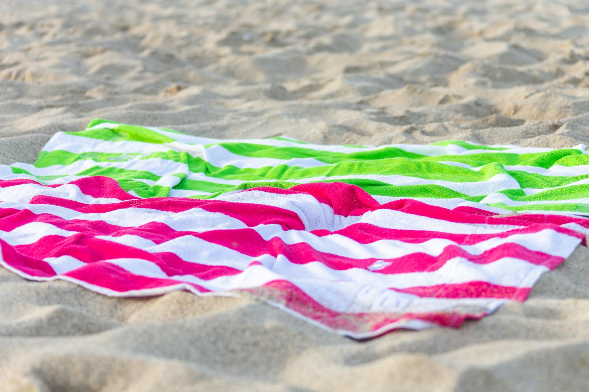 Serviettes rayées rose vif et vert sur le sable | Source : Pexels