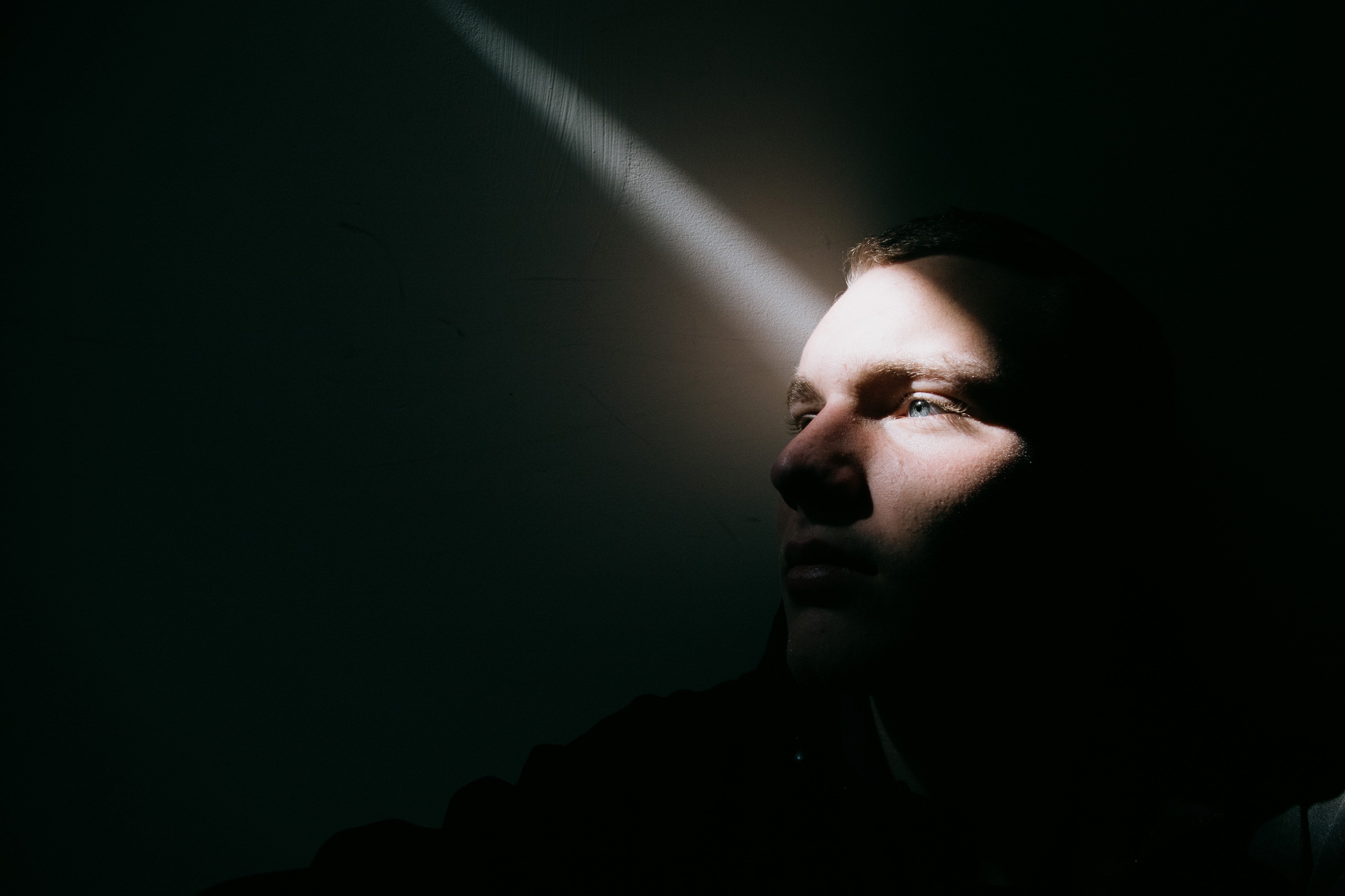 Un jeune homme bouleversé assis sur le sol d'une pièce sombre avec un filet de lumière qui s'infiltre | Source : Pexels