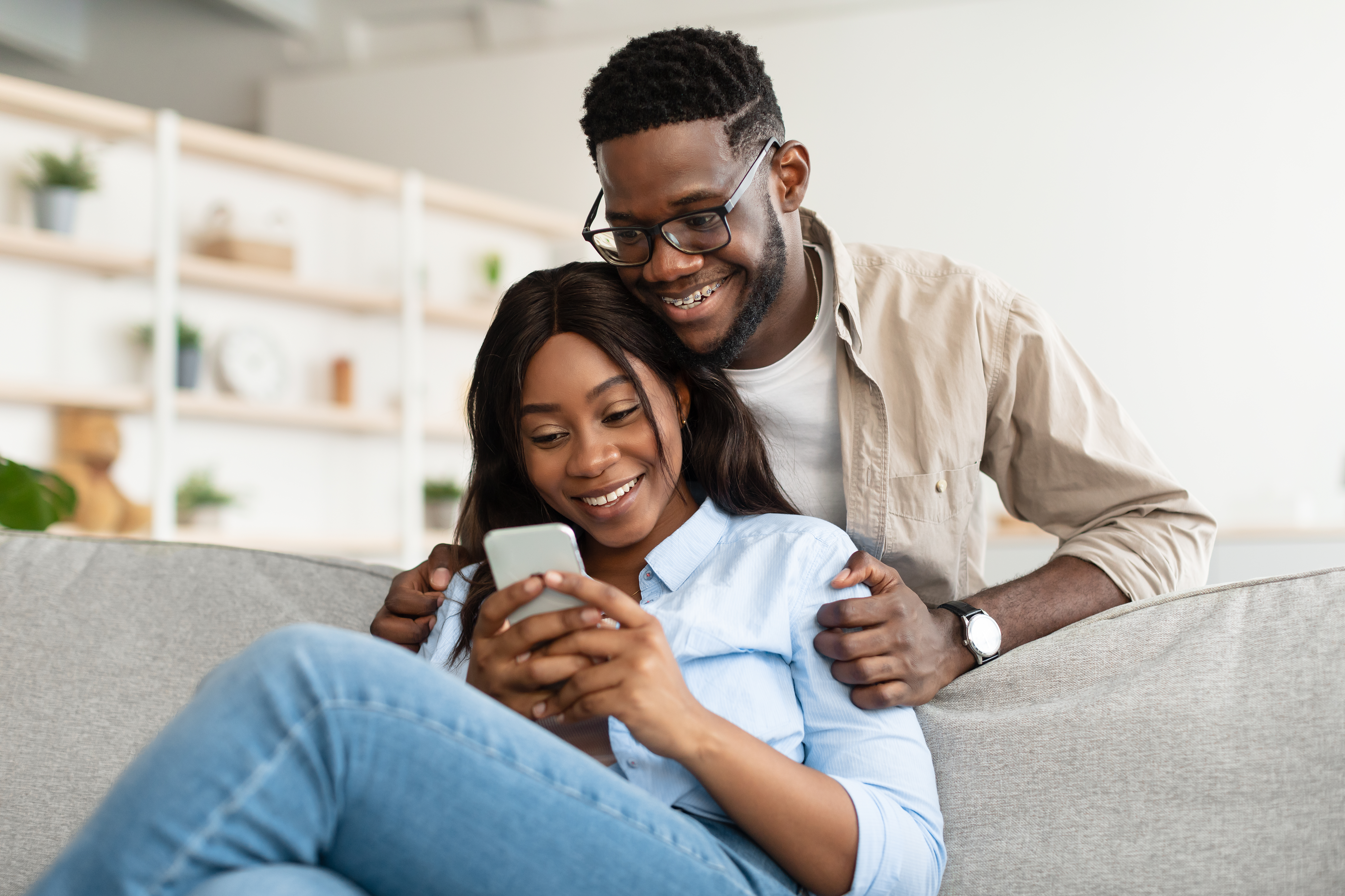 Couple afro-américain assis sur un canapé, utilisant un téléphone portable | Source : Getty Images