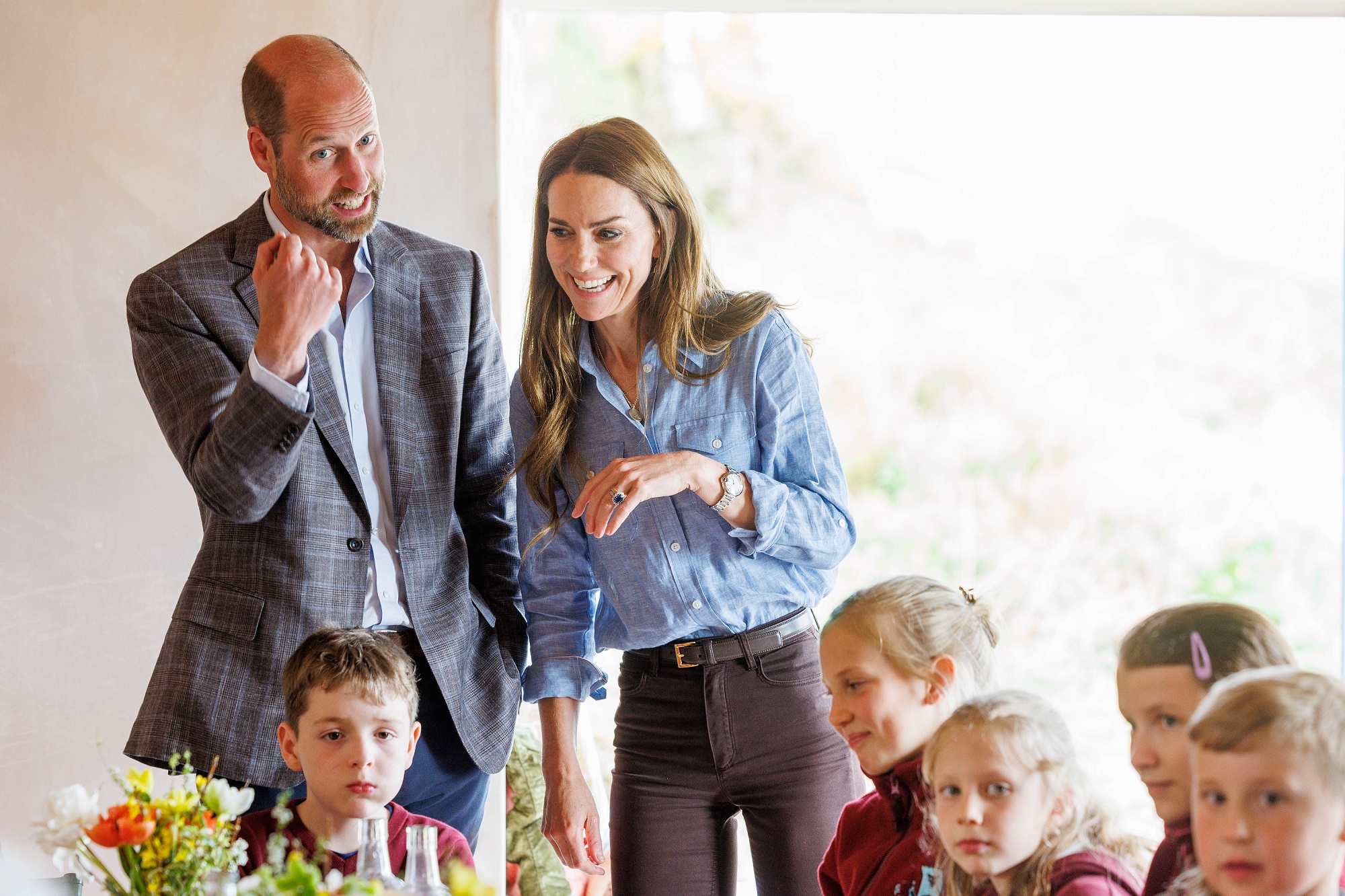 William et Catherine s'adressent à un groupe d'enfants lors d'une visite à un croft local sur la côte ouest de Mull. Tous deux sont souriants et animés, s'engageant chaleureusement avec la jeune foule.