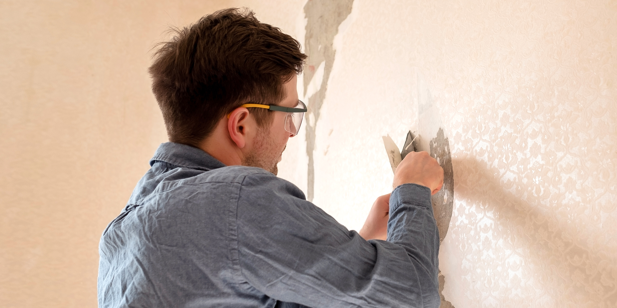 Un homme en train de décoller du papier peint | Source : Shutterstock