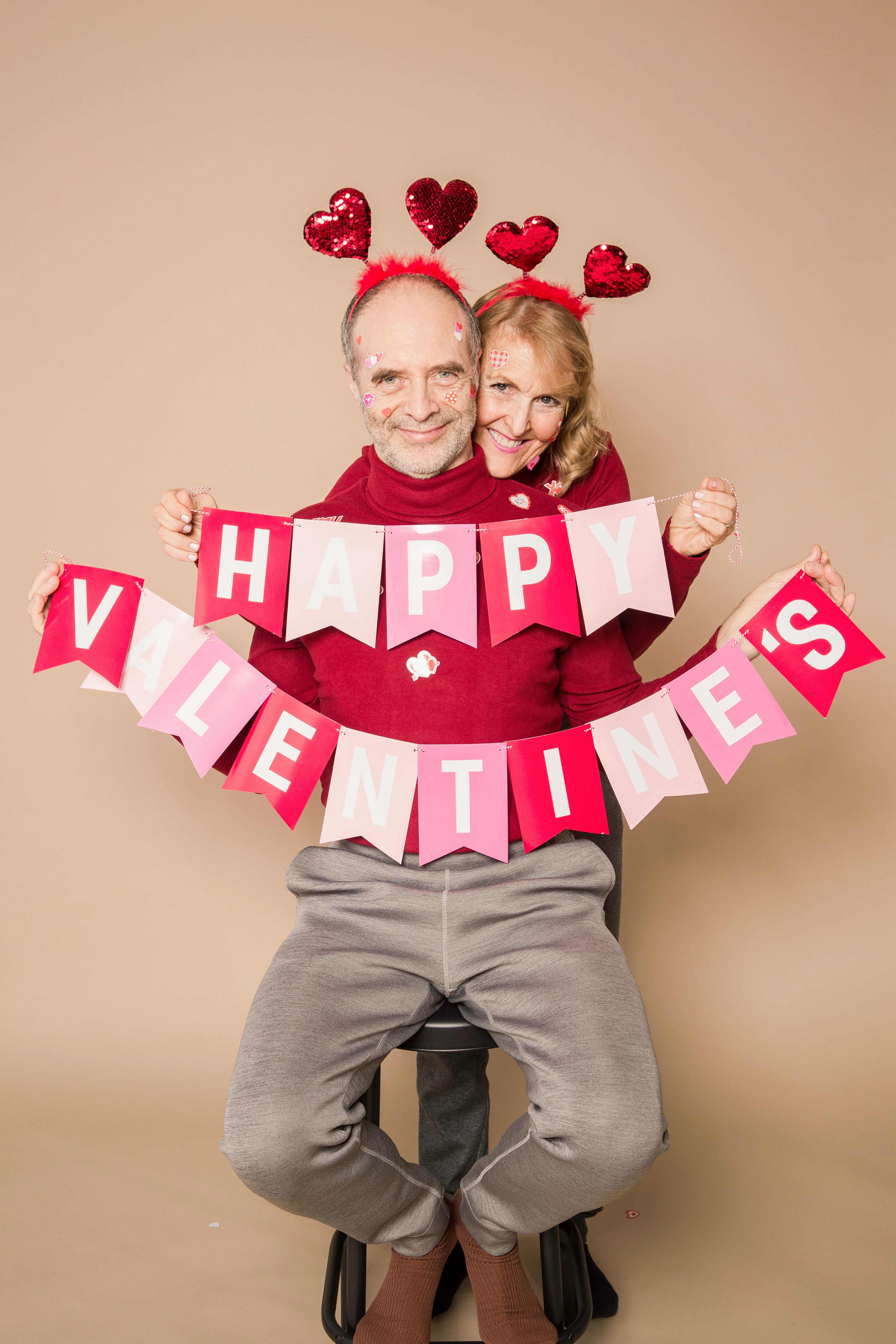 Un couple en tenue assortie tient une décoration suspendue portant l'inscription "Happy Valentine's". | Source : Pexels