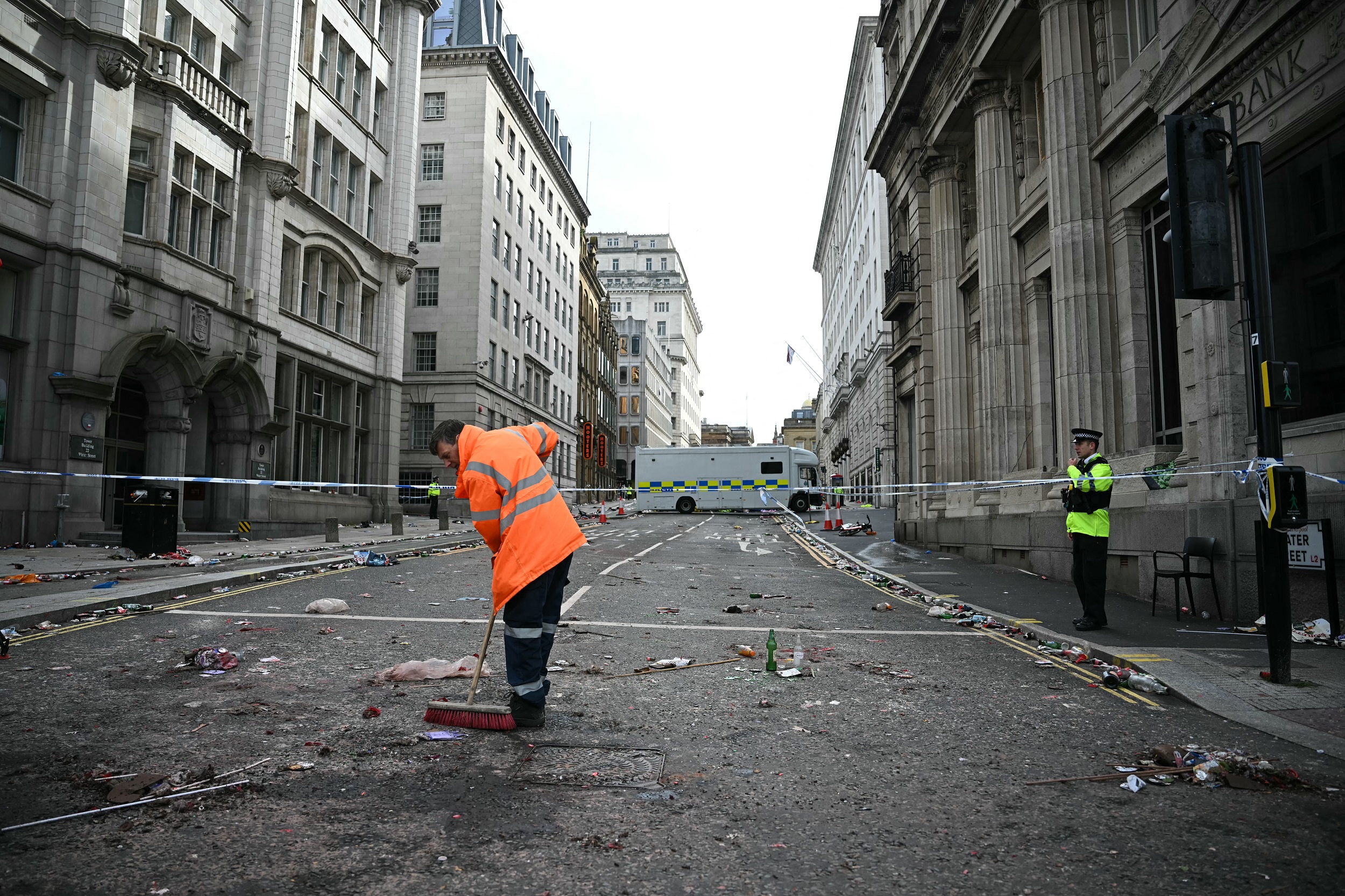 Un ouvrier nettoie les débris tandis qu'un officier de police se tient à un cordon sur Water Street à Liverpool, dans le nord-ouest de l'Angleterre, le 27 mai 2025, après qu'une voiture a foncé dans la foule qui regardait le défilé du trophée de la Premier League de Liverpool le 26 mai | Source : Getty Images