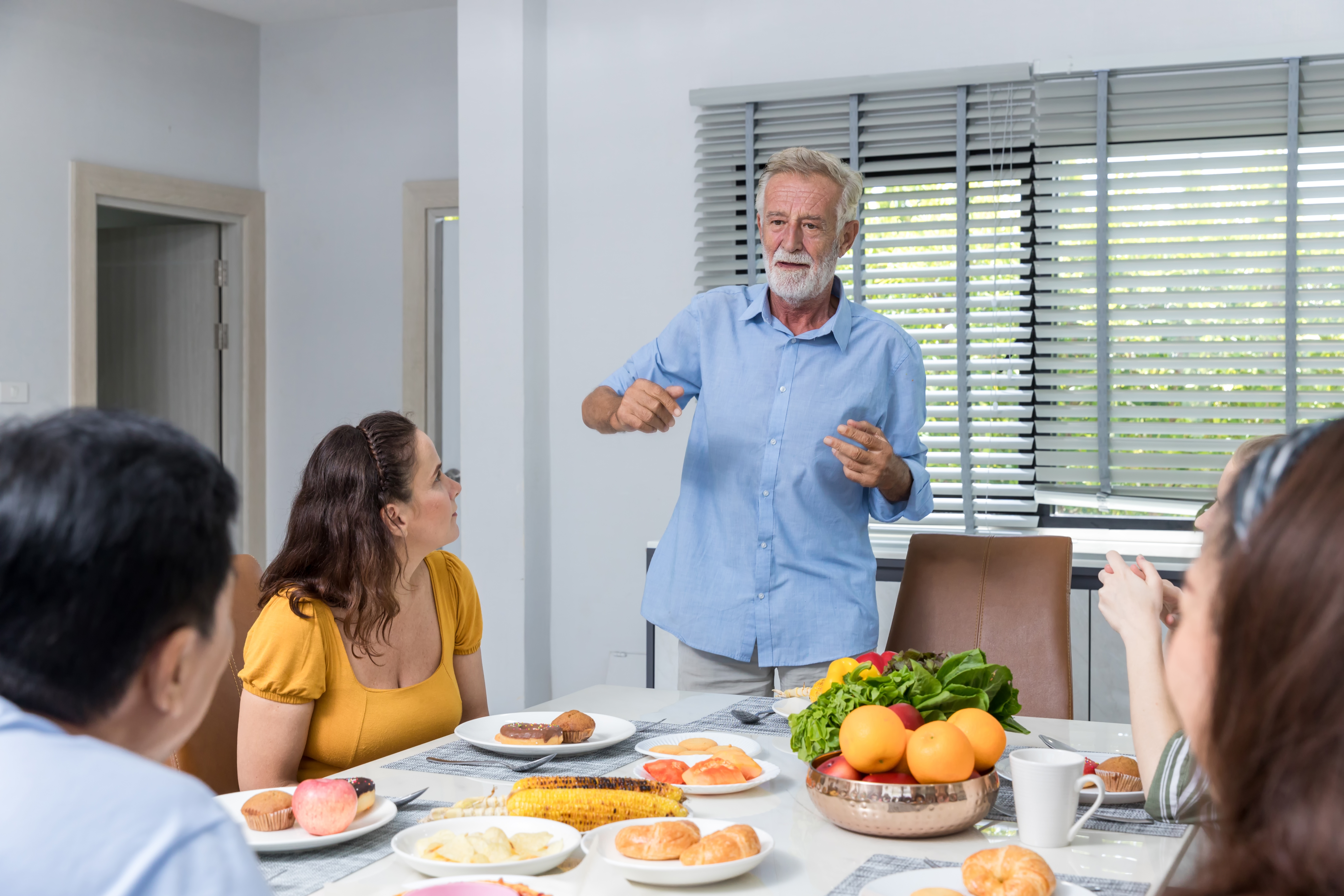Un homme âgé discutant avec sa famille pendant le dîner dans la salle à manger | Source : Shutterstock