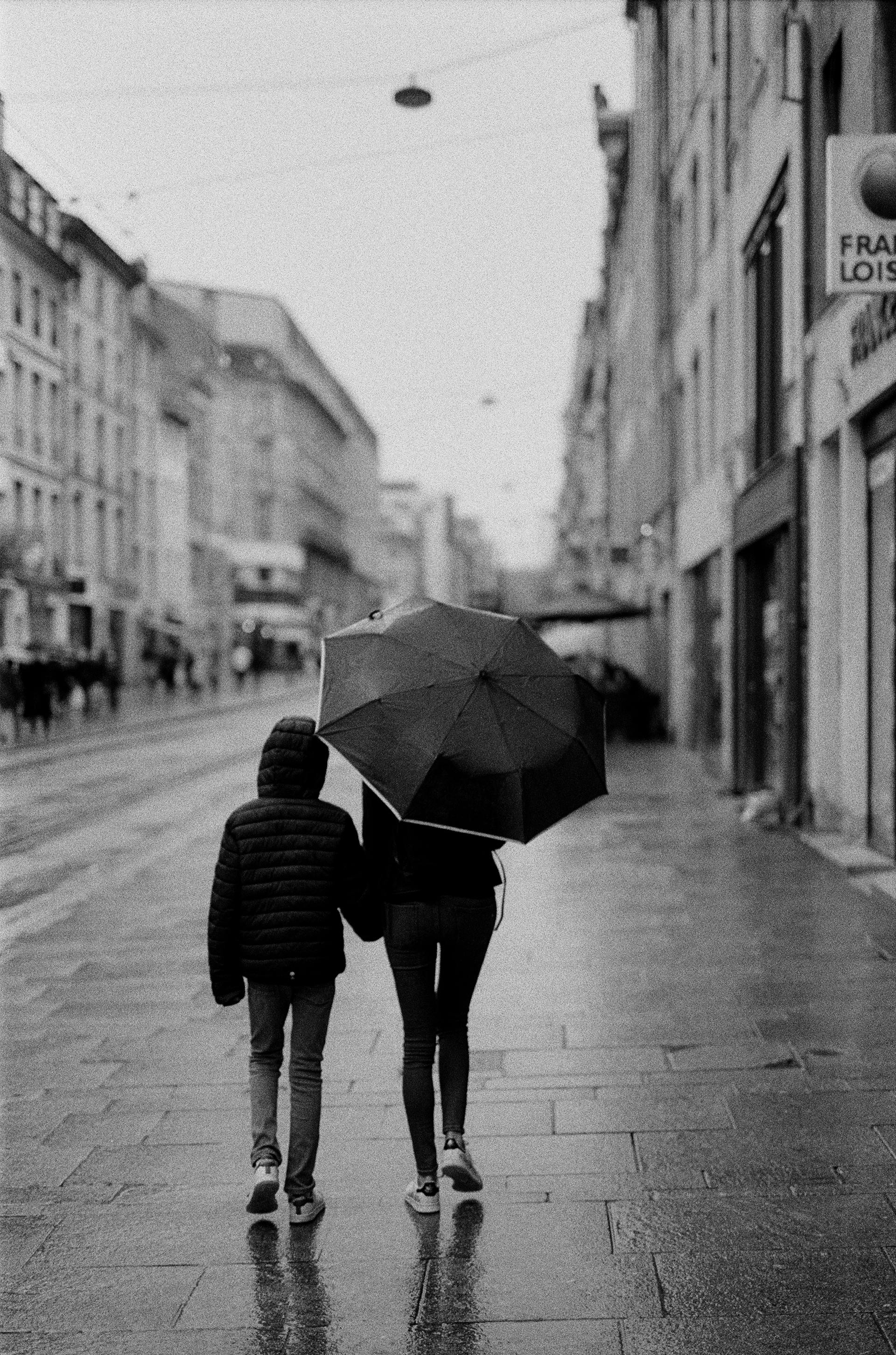 Photo en niveaux de gris d'une femme marchant avec un garçon par une journée pluvieuse | Source : Pexels