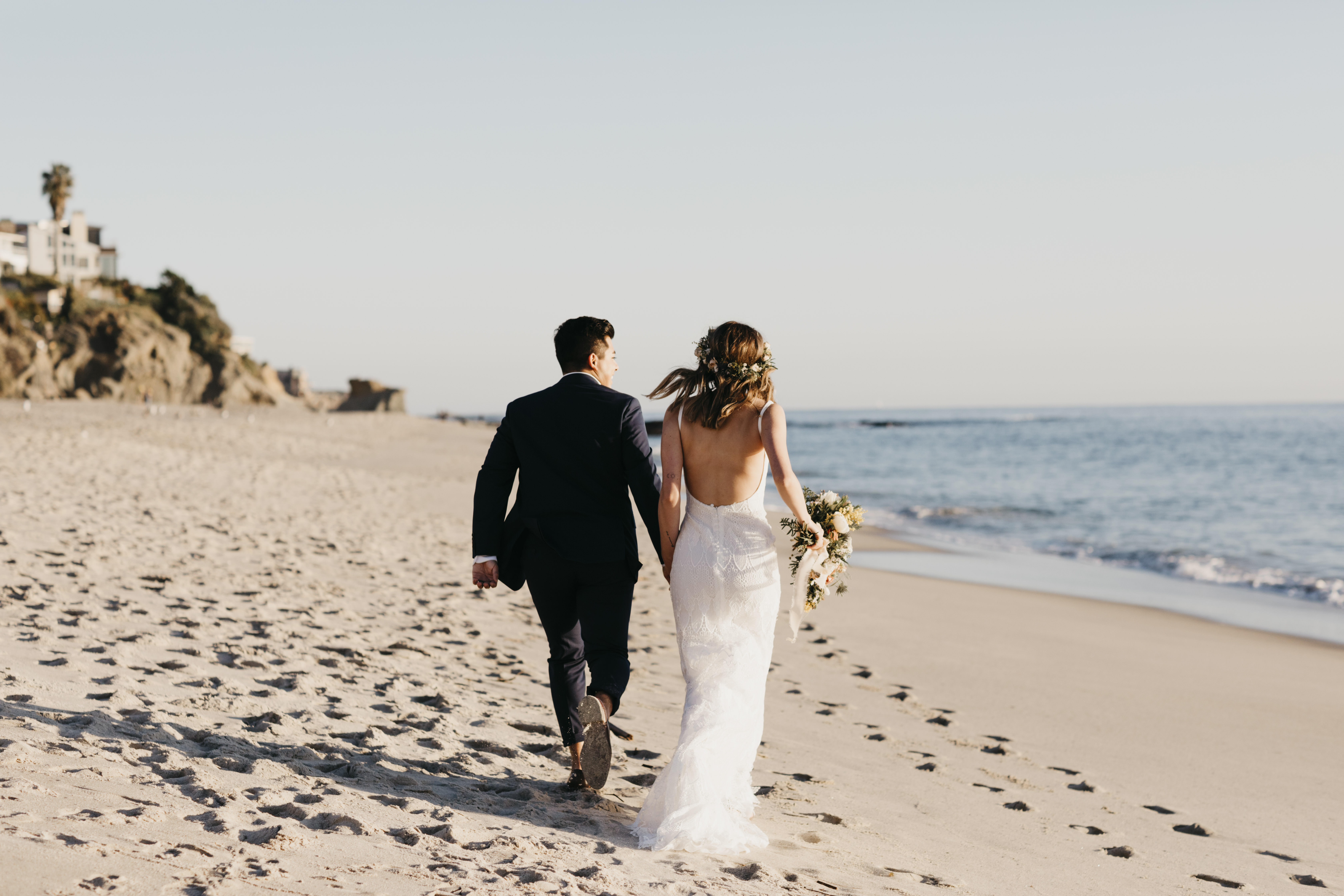 Vue arrière d'un couple de mariés heureux courant sur la plage | Source : Getty Images