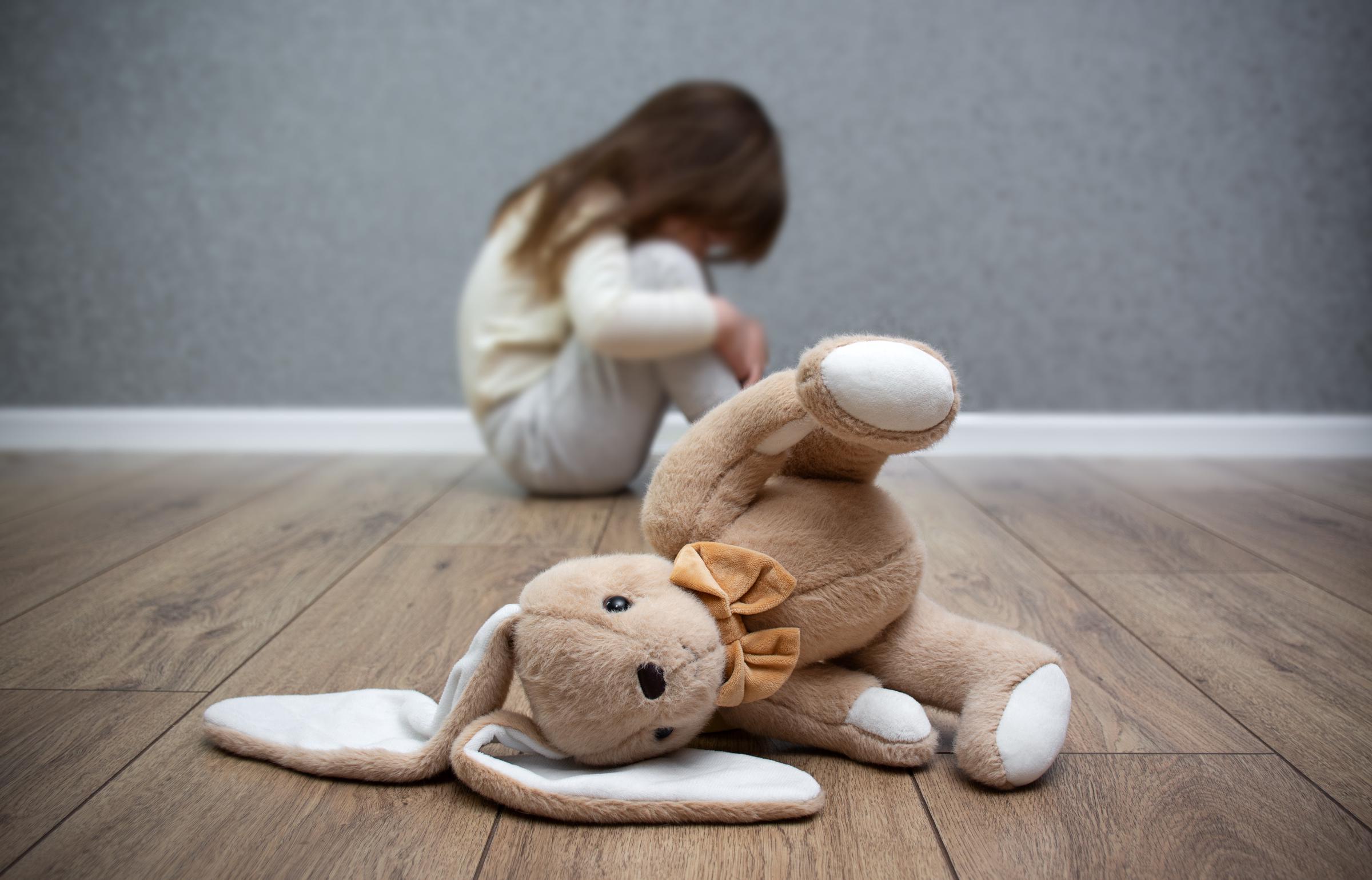 Un lapin en peluche par terre, un enfant effrayé assis derrière. Maltraitance infantile I Photo d'illustration I Source : Getty Images