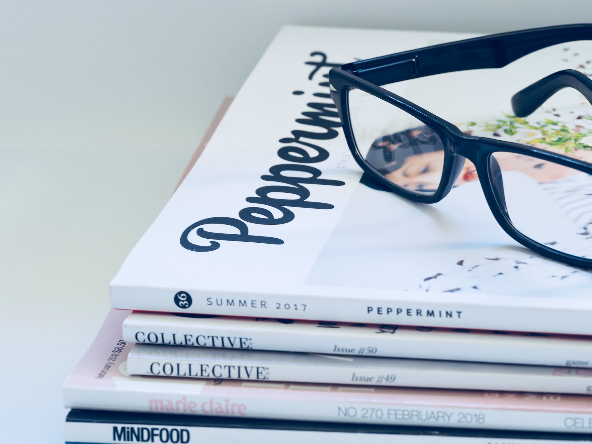 Une paire de lunettes de soleil noires posée sur une pile de magazines | Source : Pexels