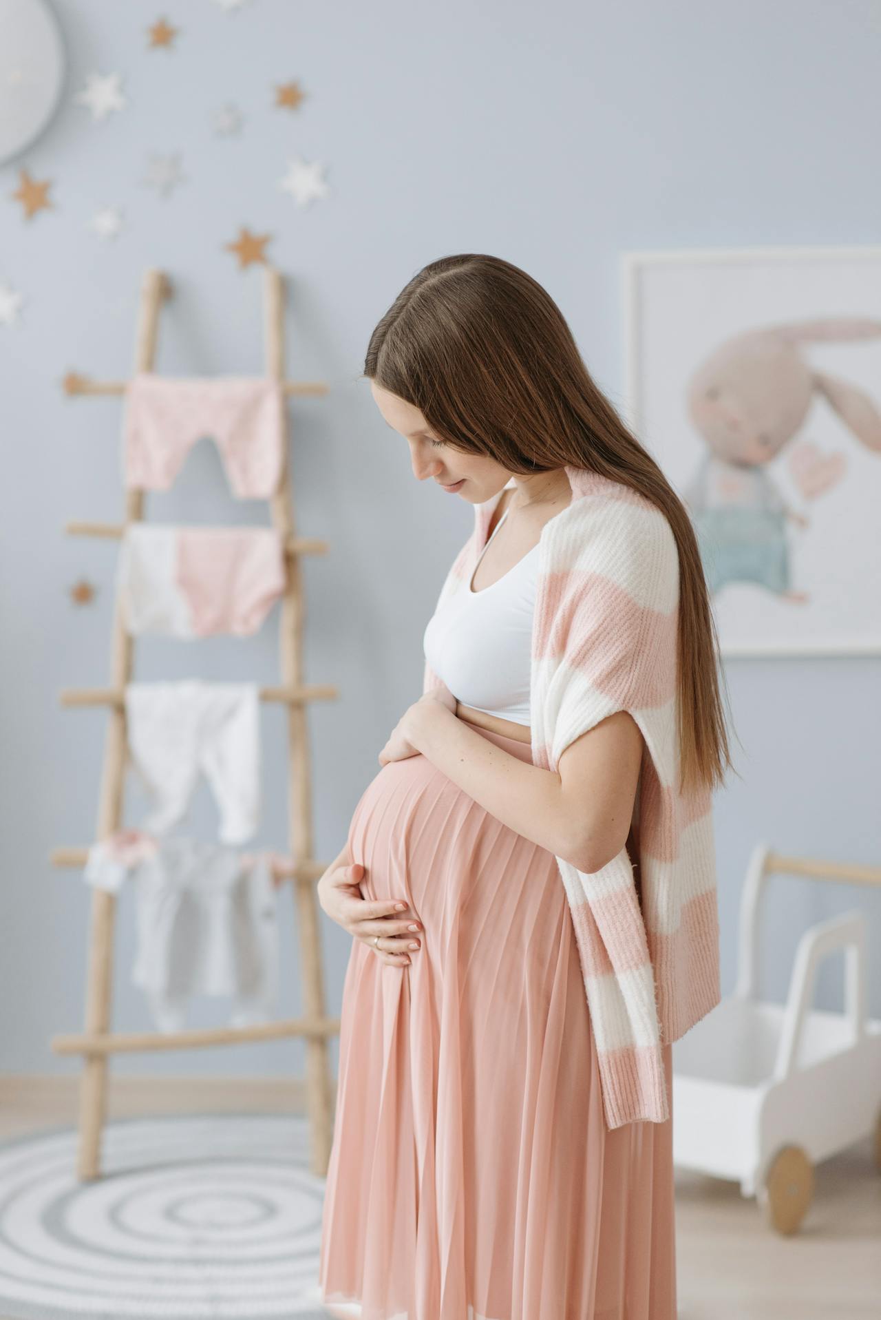 Une femme enceinte frotte son baby bump tout en se tenant dans une chambre d'enfant peinte dans une nuance de bleu pâle | Source : Pexels