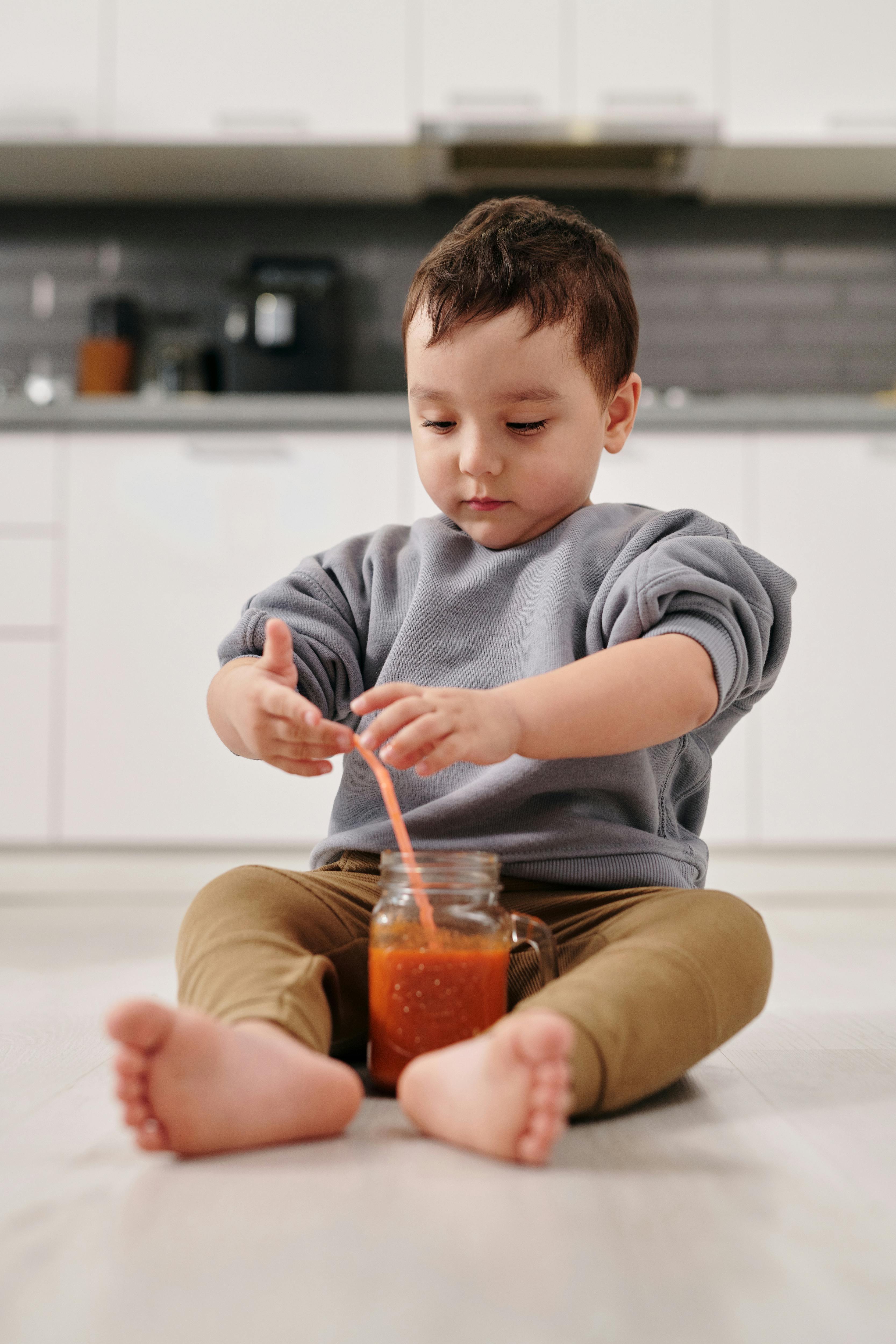 Un enfant assis par terre à côté d'un verre de jus de fruit avec une paille | Source : Pexels