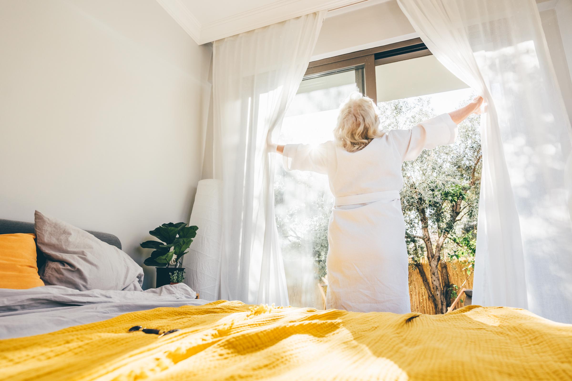 Une femme ouvrant les rideaux de sa chambre | Source : Getty Images