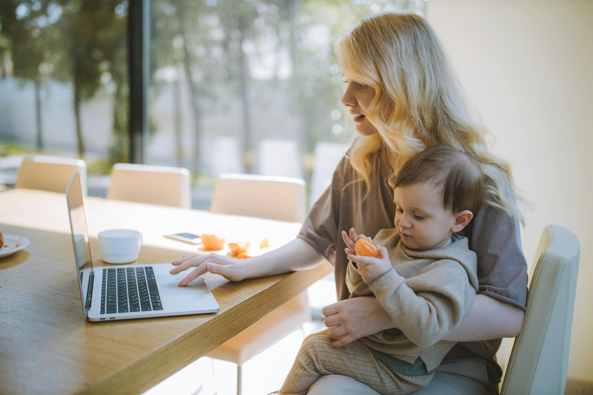 Une femme portant son fils tout en utilisant un ordinateur portable | Source : Pexels