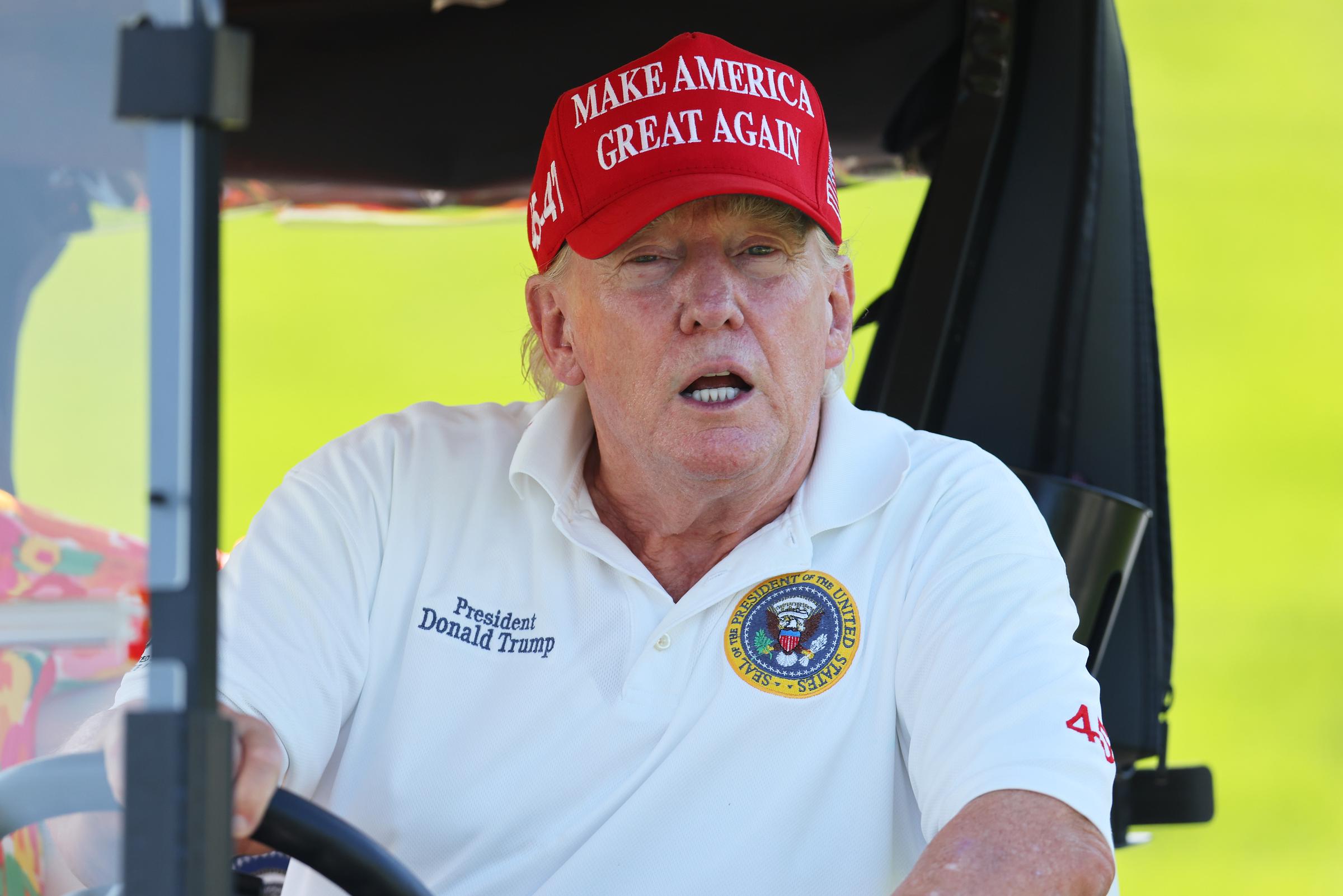 Lors de l'événement de Bedminster, dans le New Jersey, le 11 août, Donald Trump est assis à l'intérieur d'une voiturette de golf, vêtu d'un polo blanc avec un emblème présidentiel. Son visage apparaît plus rouge que son cou, surtout sous la lumière vive de l'extérieur.