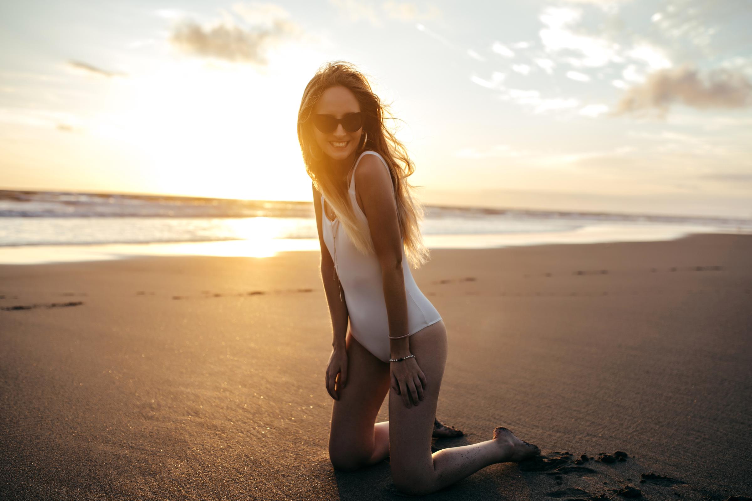 Une femme en maillot de bain blanc agenouillée sur la plage | Source : Freepik