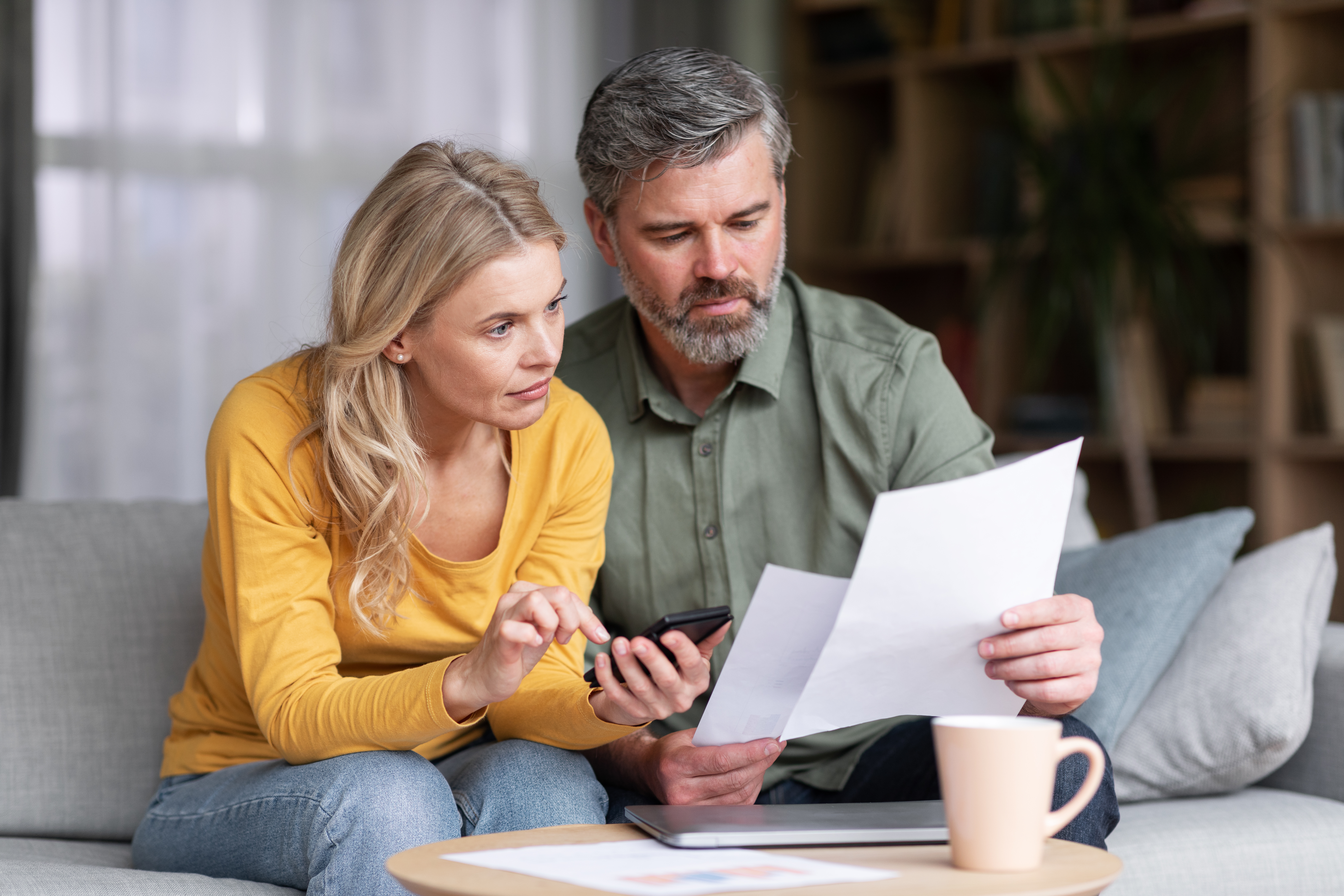 Couple marié d'âge moyen planifiant un budget ensemble, lisant des documents et calculant les dépenses | Source : Getty Images