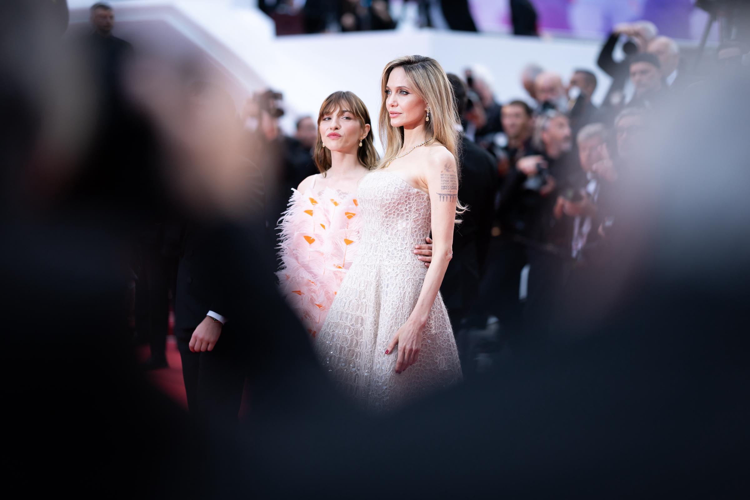 Encadrées par des silhouettes floues au premier plan, Angelina Jolie et Marie Colomb partagent un moment saisissant sur le tapis rouge. Angelina Jolie se tient debout dans sa robe à paillettes Cucinelli, tandis que Marie Colomb est stupéfiante dans une mini robe à plumes d'inspiration florale, les deux femmes attirant l'attention sous tous les angles.