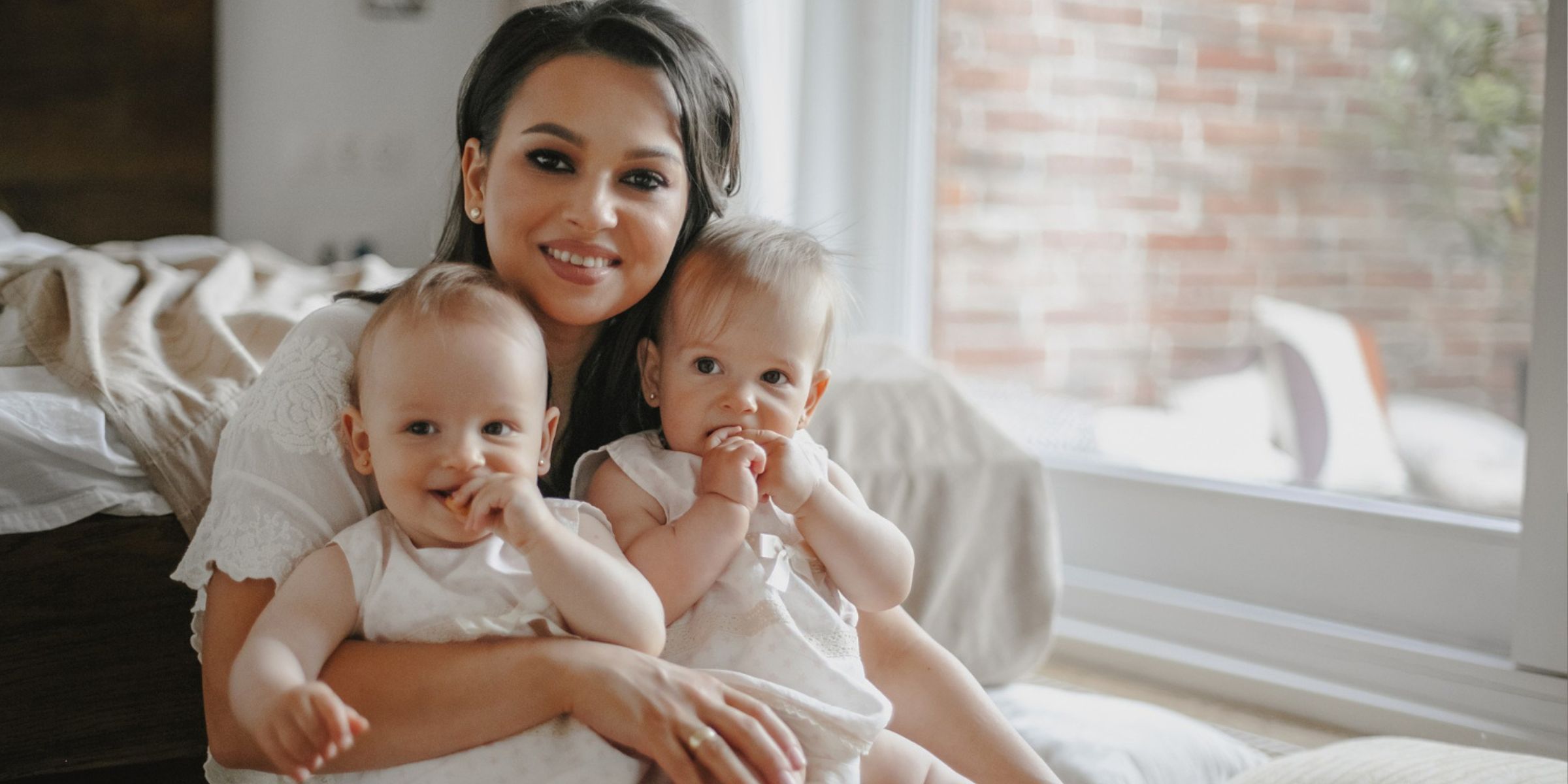 Une maman qui sourit en tenant dans ses bras deux bébés | Source : Magnific