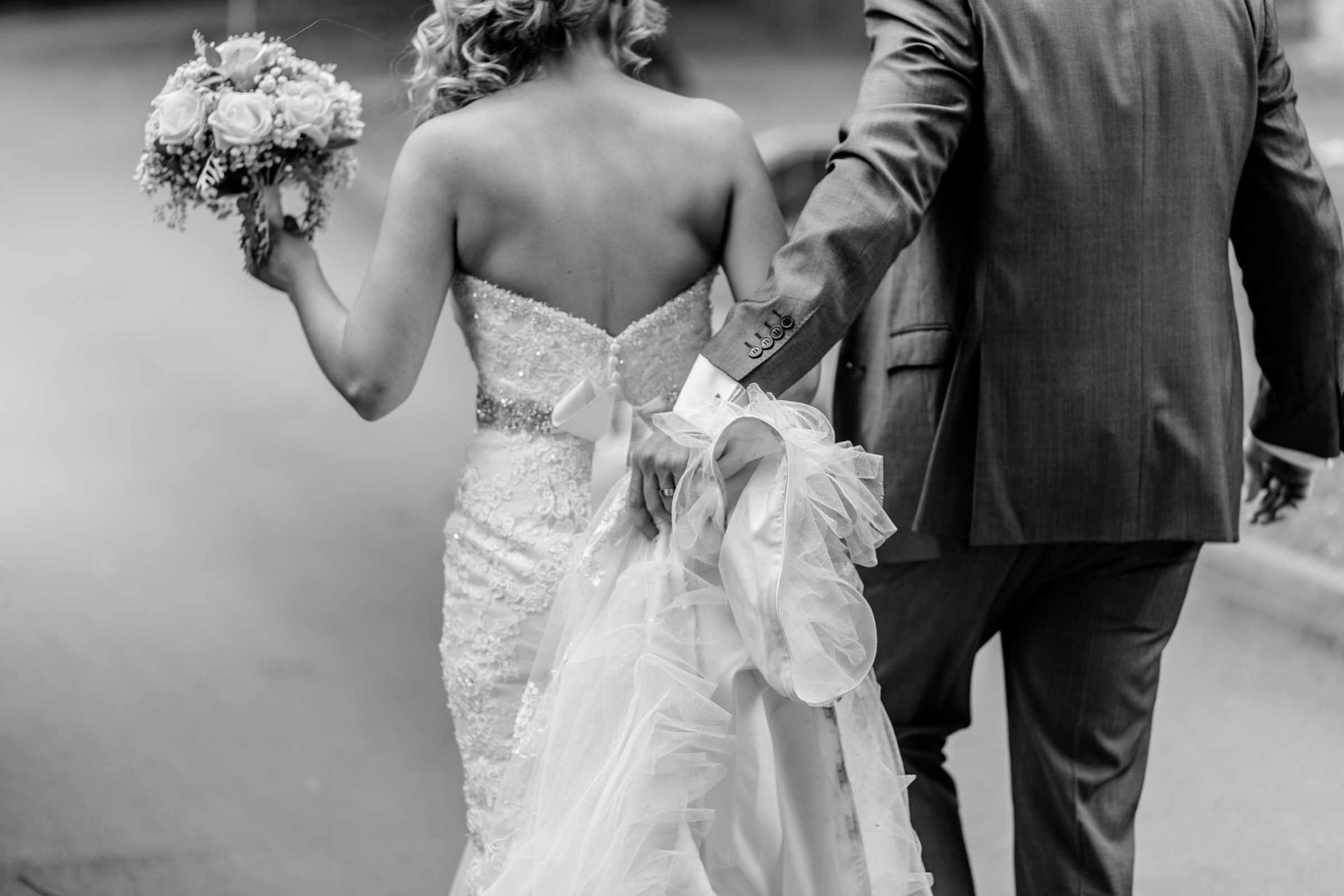 Niveaux de gris d'une mariée et d'un marié marchant ensemble | Source : Unsplash