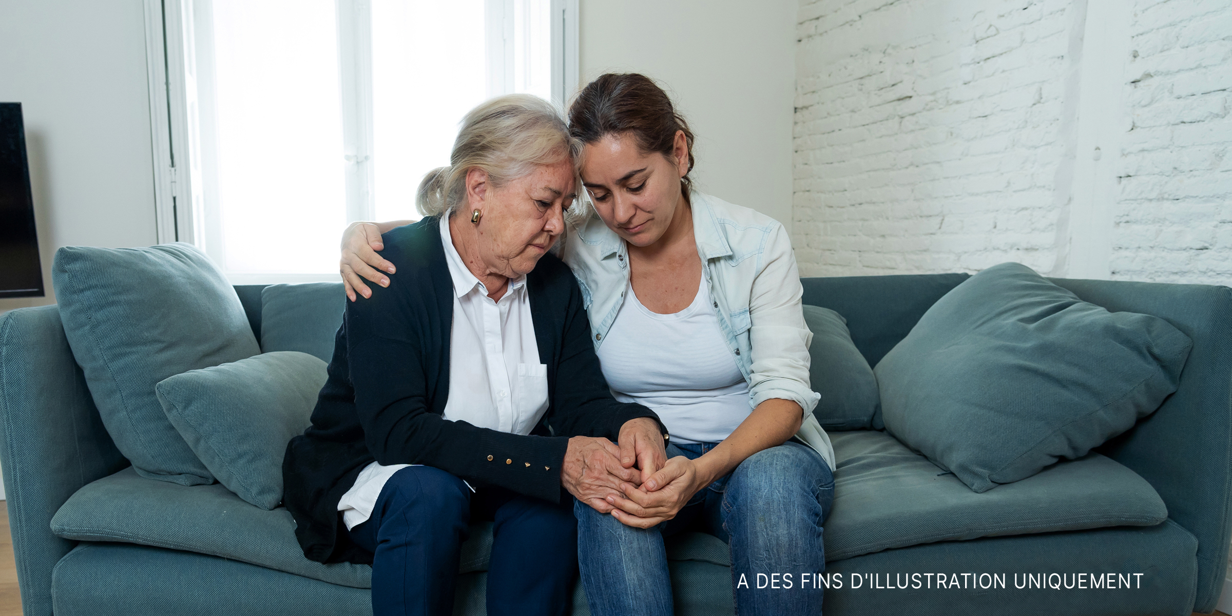 Une femme âgée tenant la main d'une autre plus jeune et les deux sont assises sur un canapé. | Source : Shutterstock