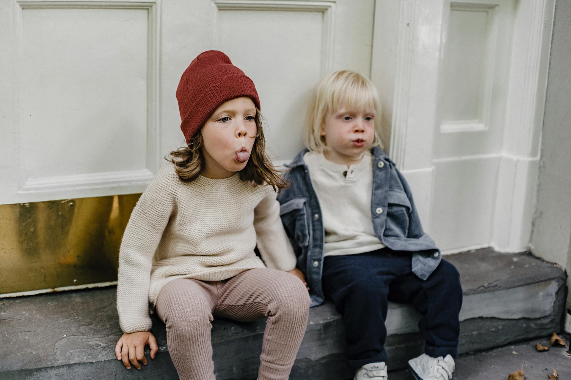 Deux enfants assis sous le porche font des grimaces | Source : Pexels