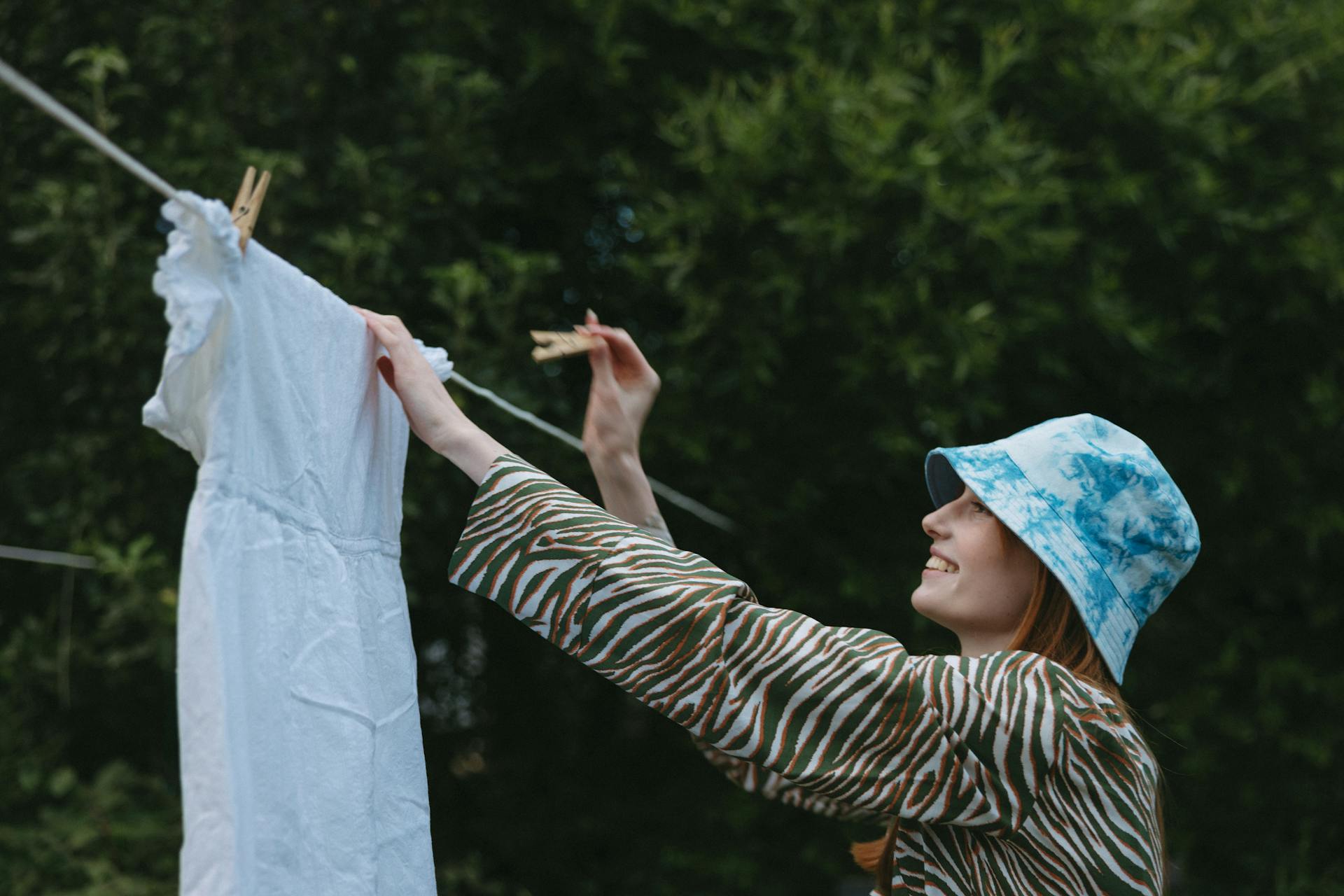 Une femme souriante accroche une robe sur une corde à linge | Source : Pexels