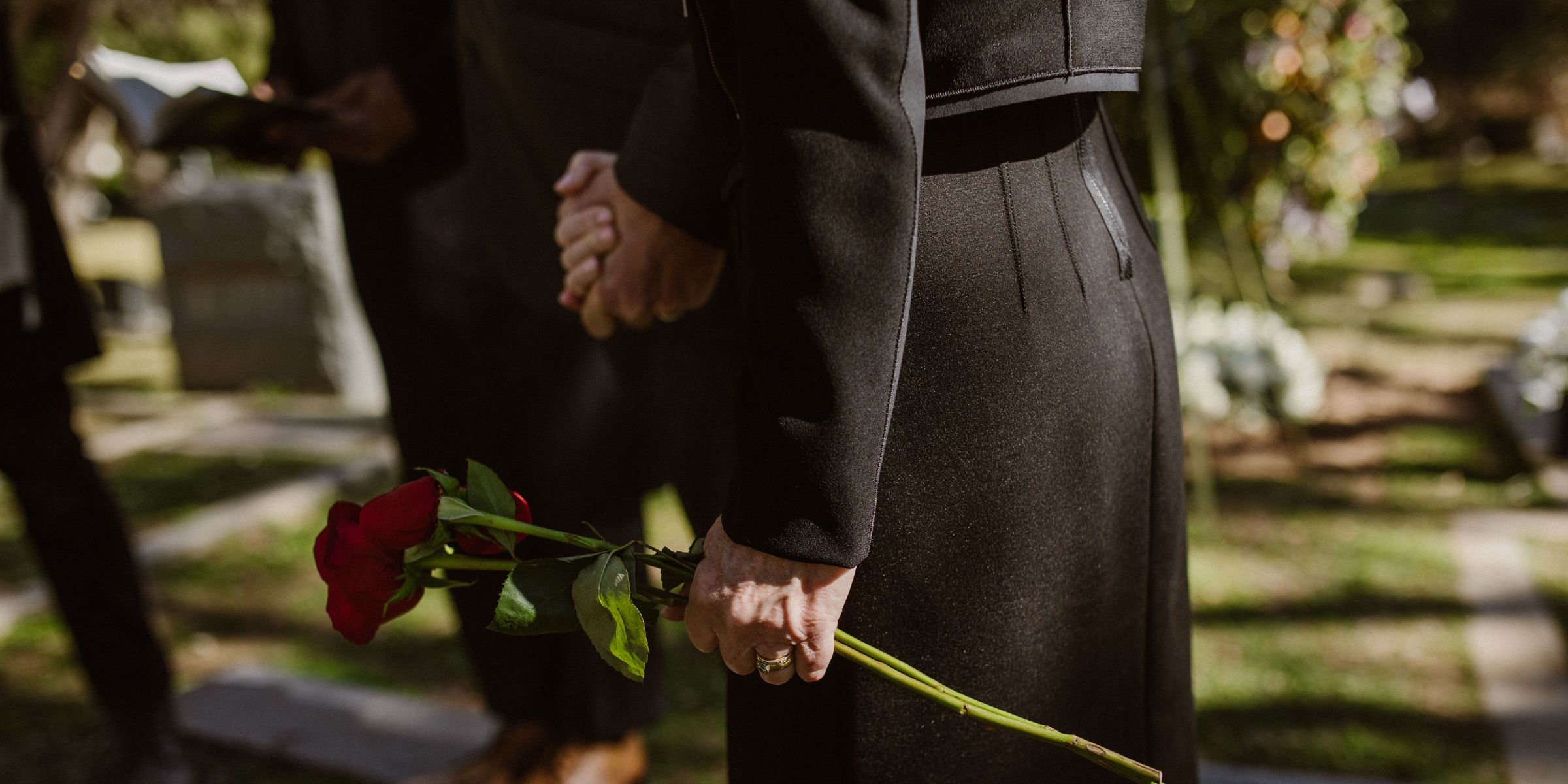 Gros plan sur une femme habillée en noir tenant une rose rouge dans un cimetière | Source : Pexels