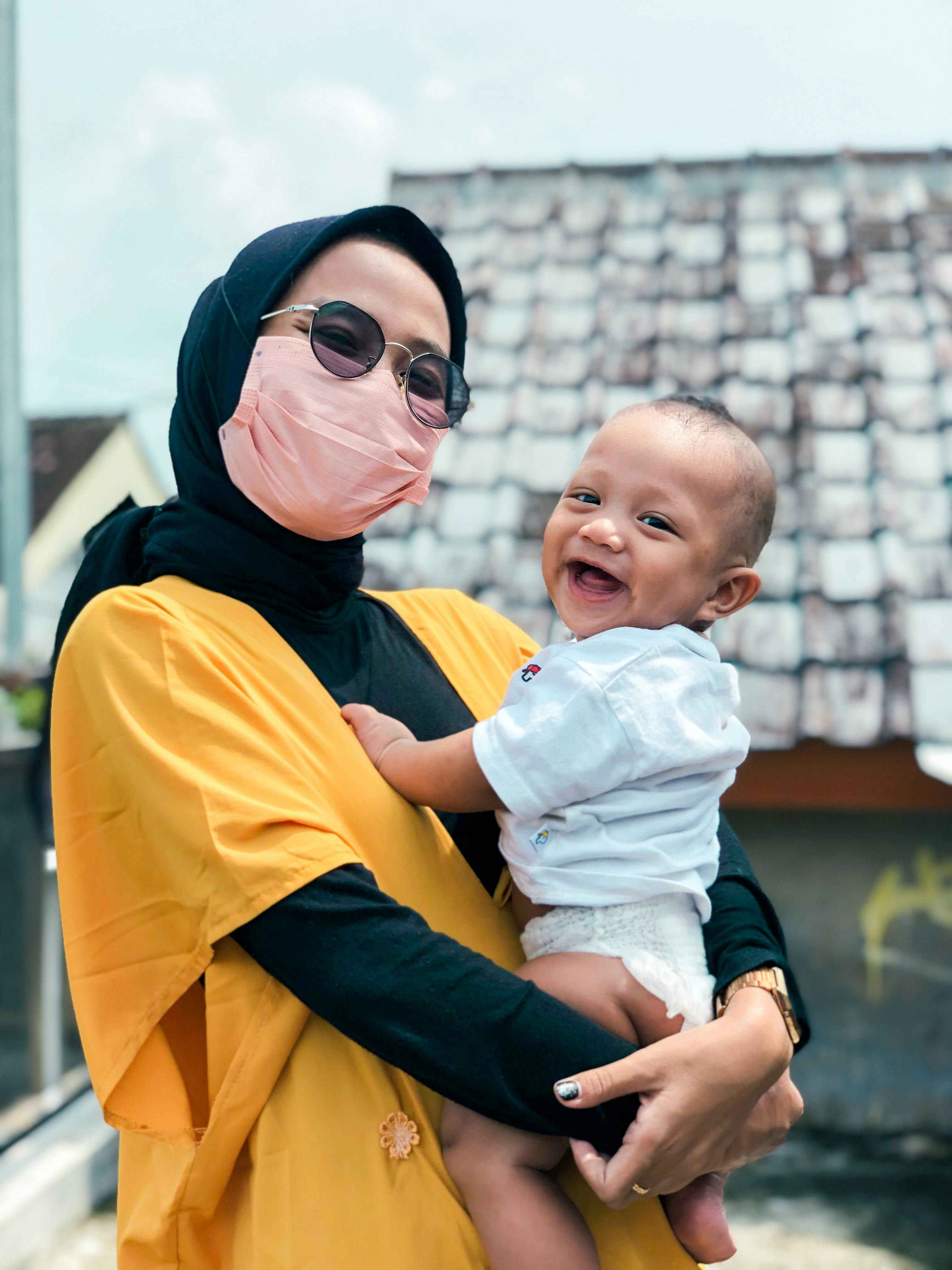 Une femme portant un masque et tenant un bébé souriant | Source : Pexels