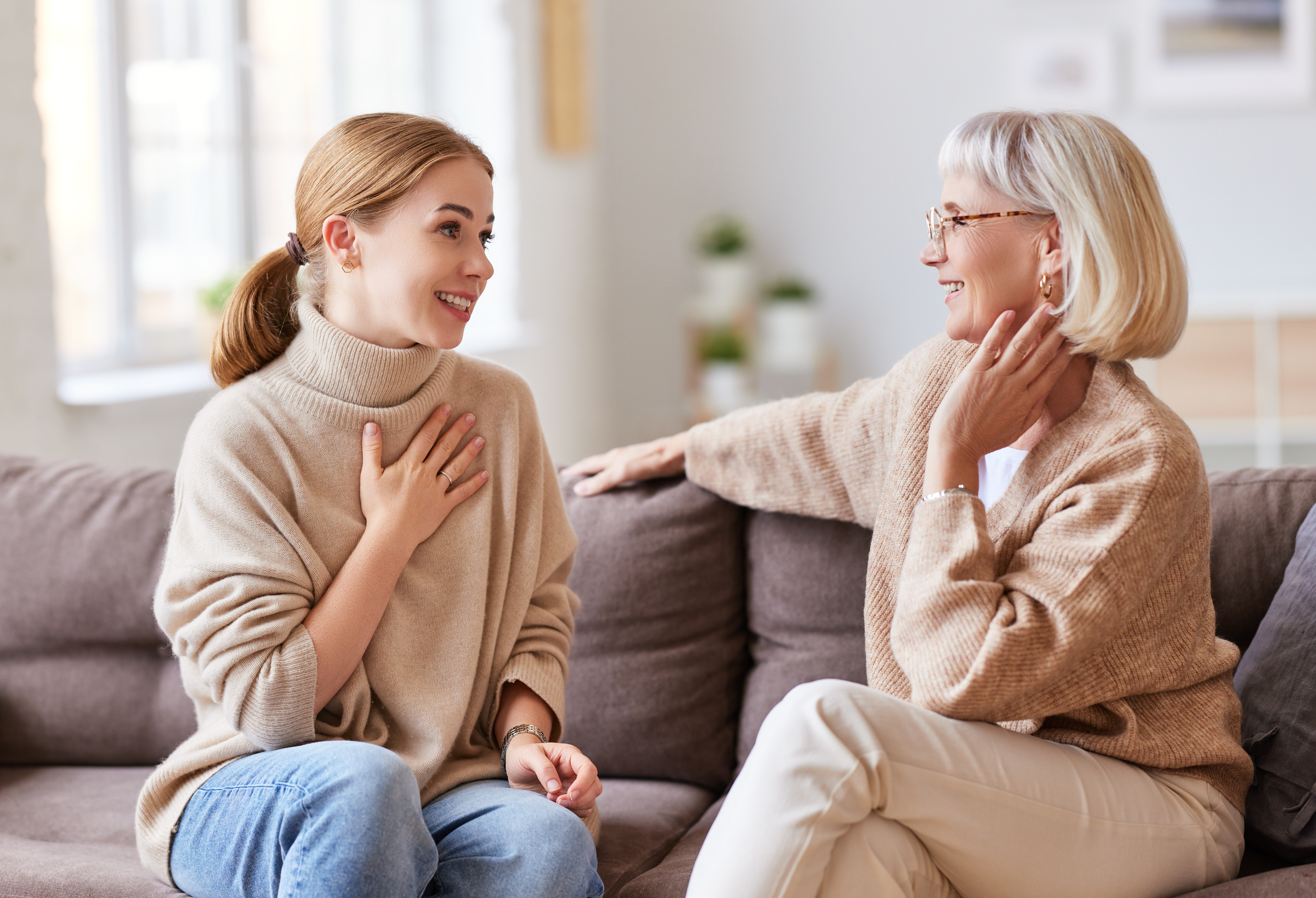 Une jeune femme sourit tout en parlant à une personne plus âgée, assise sur un canapé | Source : Shutterstock