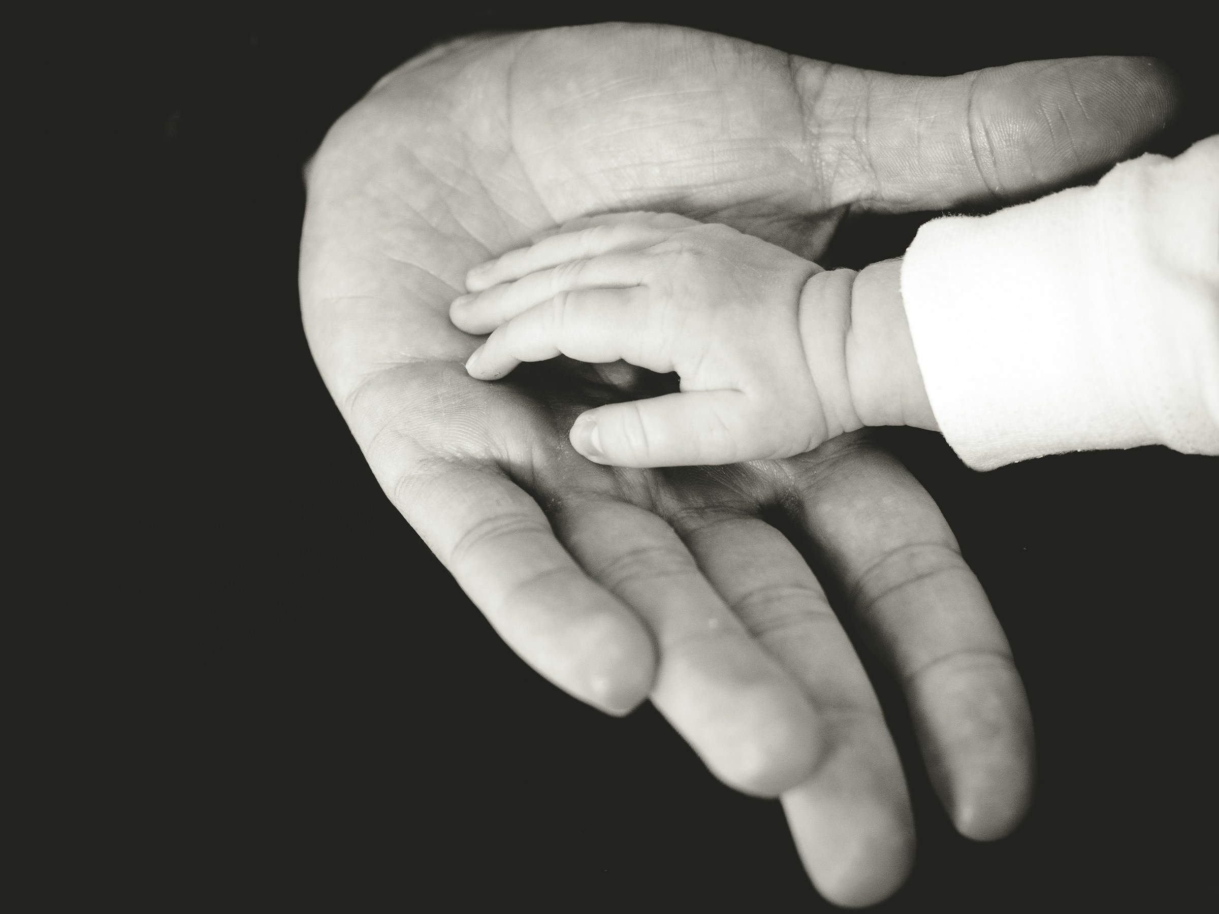 Photographie en niveaux de gris d'un parent tenant la main de son bébé | Source : Unsplash