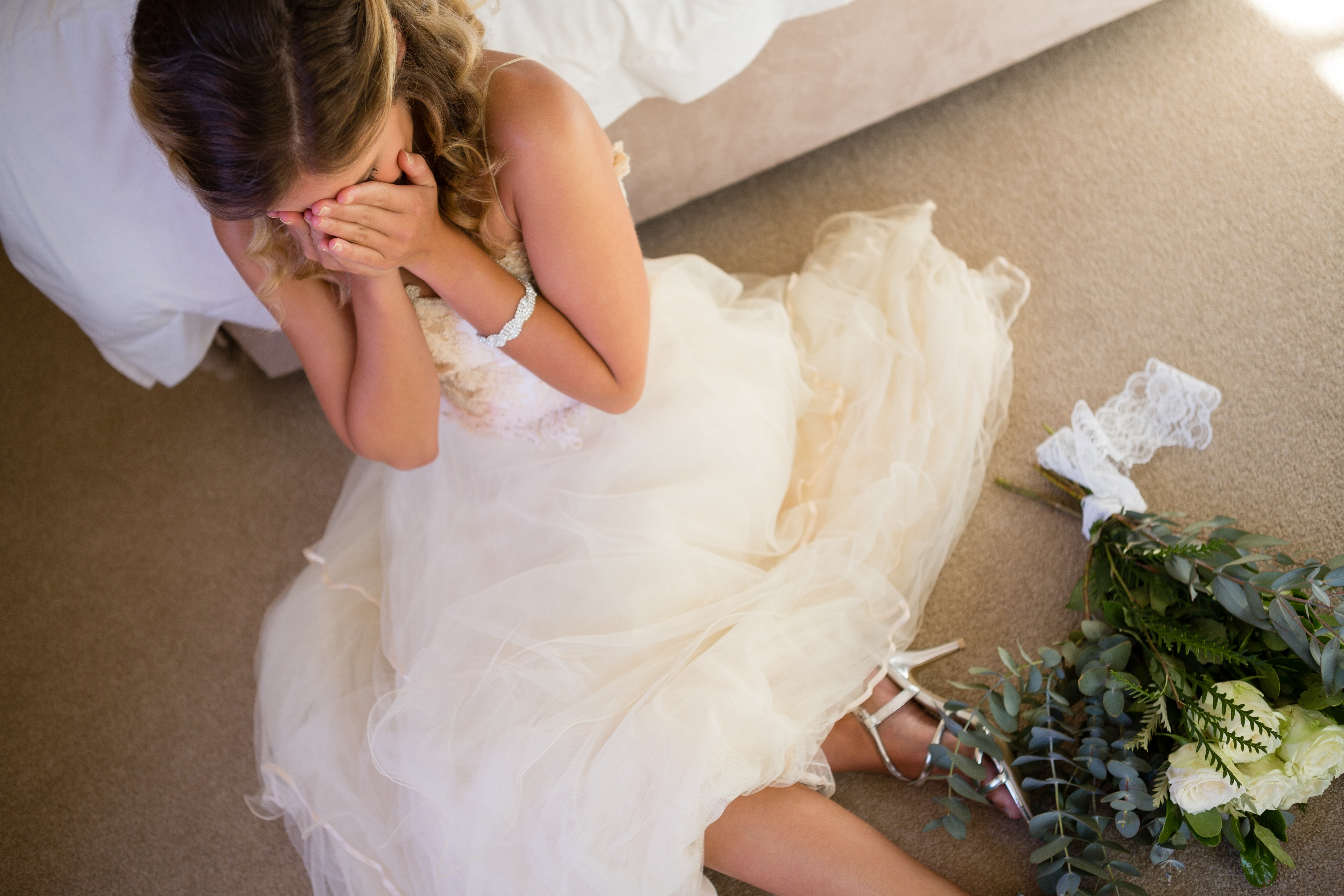 Une mariée qui pleure sur le sol en s'appuyant sur un lit | Source : Shutterstock