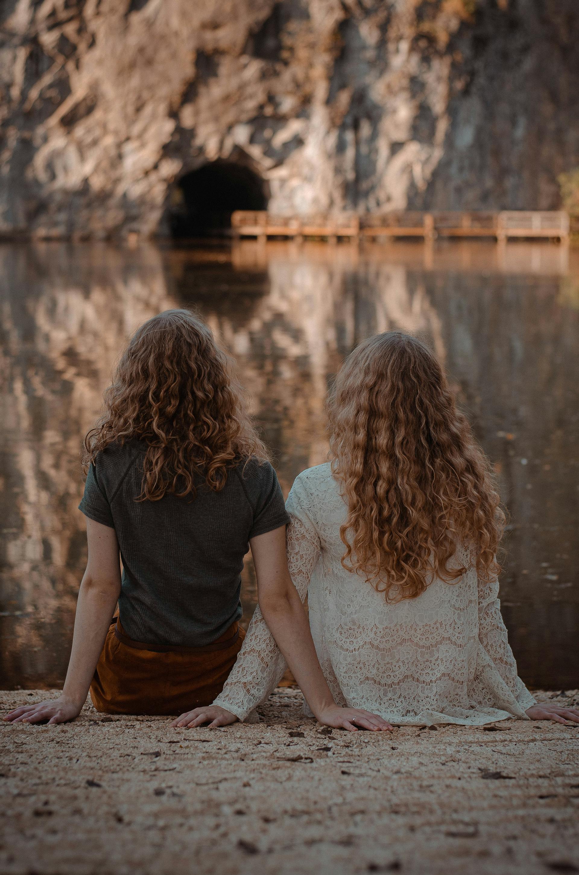 Deux femmes assises sur le sol face à un plan d'eau | Source : Pexels