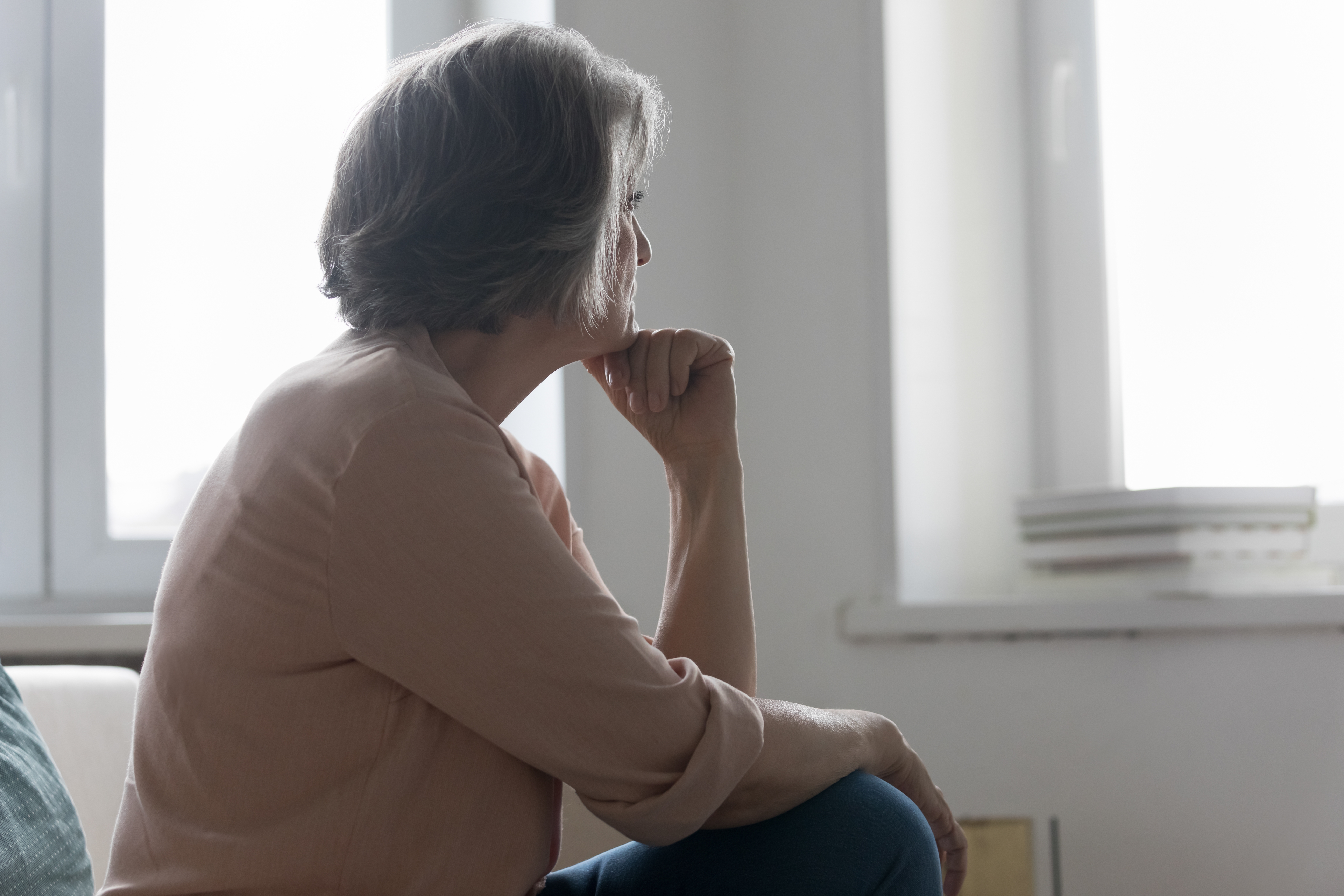 Une femme âgée regarde avec nostalgie la fenêtre alors que quelqu'un lui manque | Source : Shutterstock