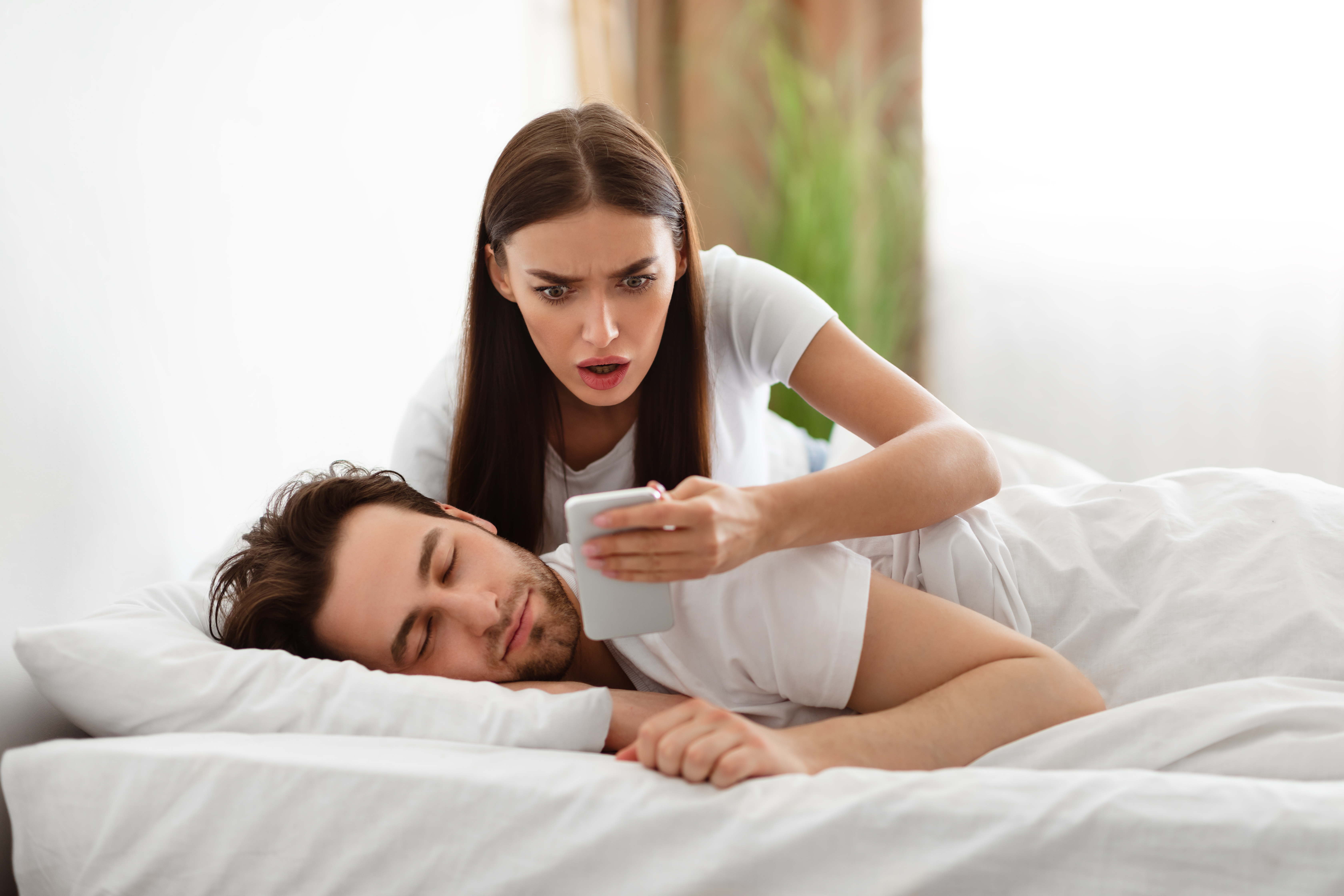 Femme choquée lisant un message sur le téléphone de son partenaire. | Source : Shutterstock
