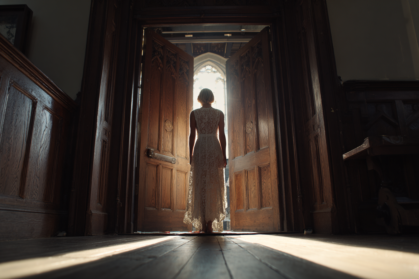 Une femme portant une robe en dentelle blanche se tient dans l'embrasure d'une porte | Source : Midjourney