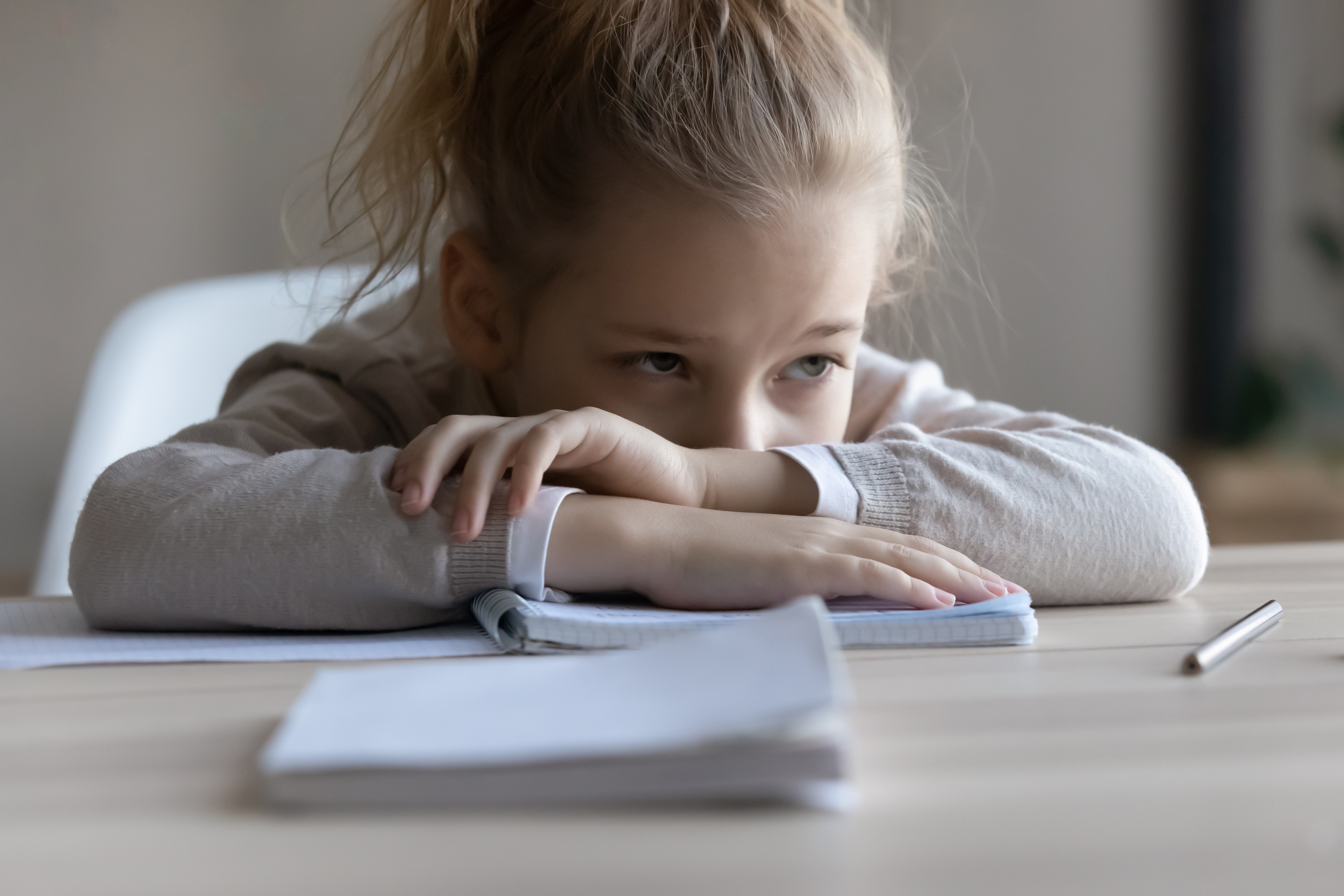 Une petite fille triste pose sa tête sur la table, distraite par son travail | Source : Shutterstock