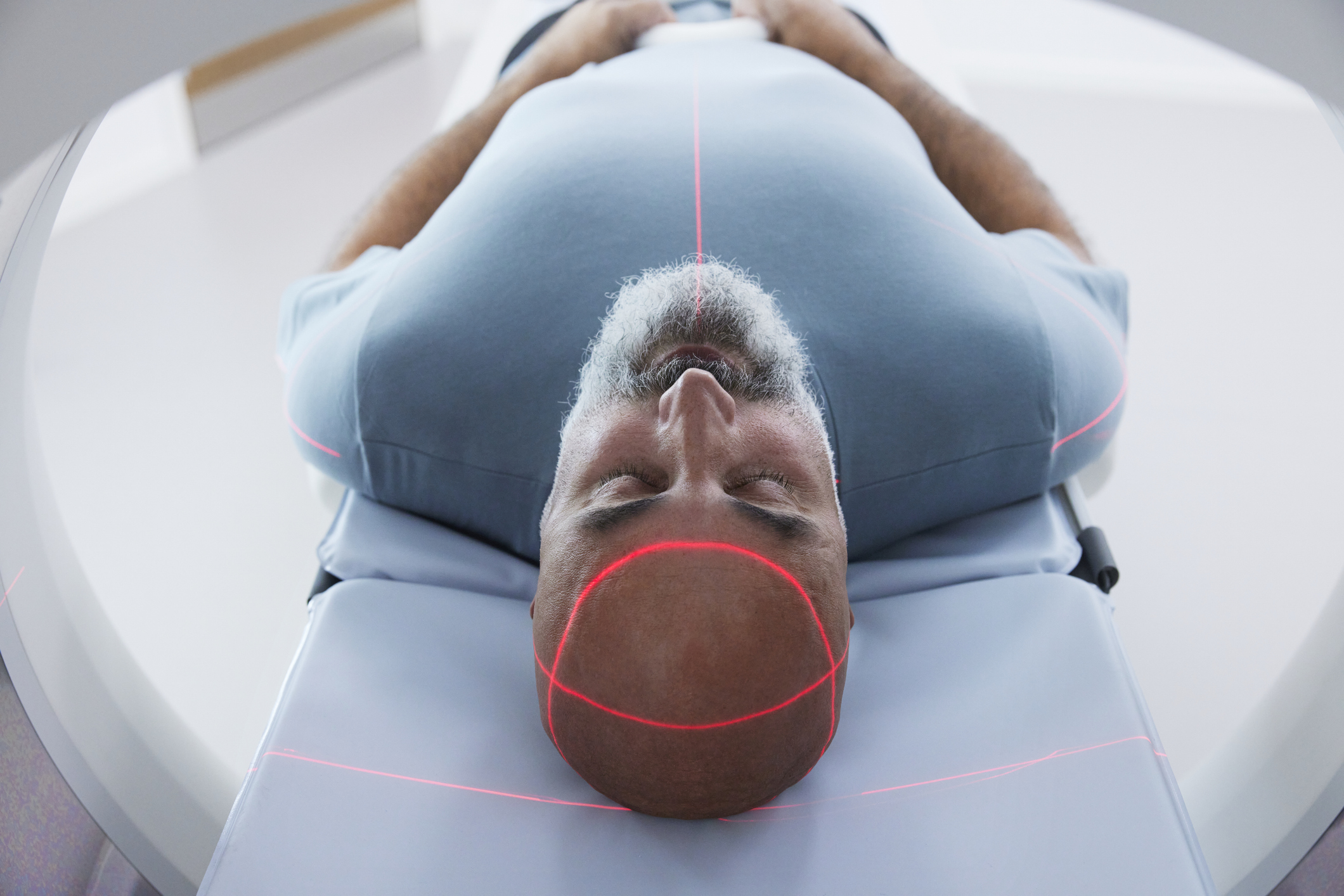 Homme subissant un scanner cérébral à l'intérieur d'un appareil de tomodensitométrie ou d'IRM, avec des lasers rouges assurant un alignement correct pour détecter des tumeurs ou d'autres anomalies | Source : Getty Images