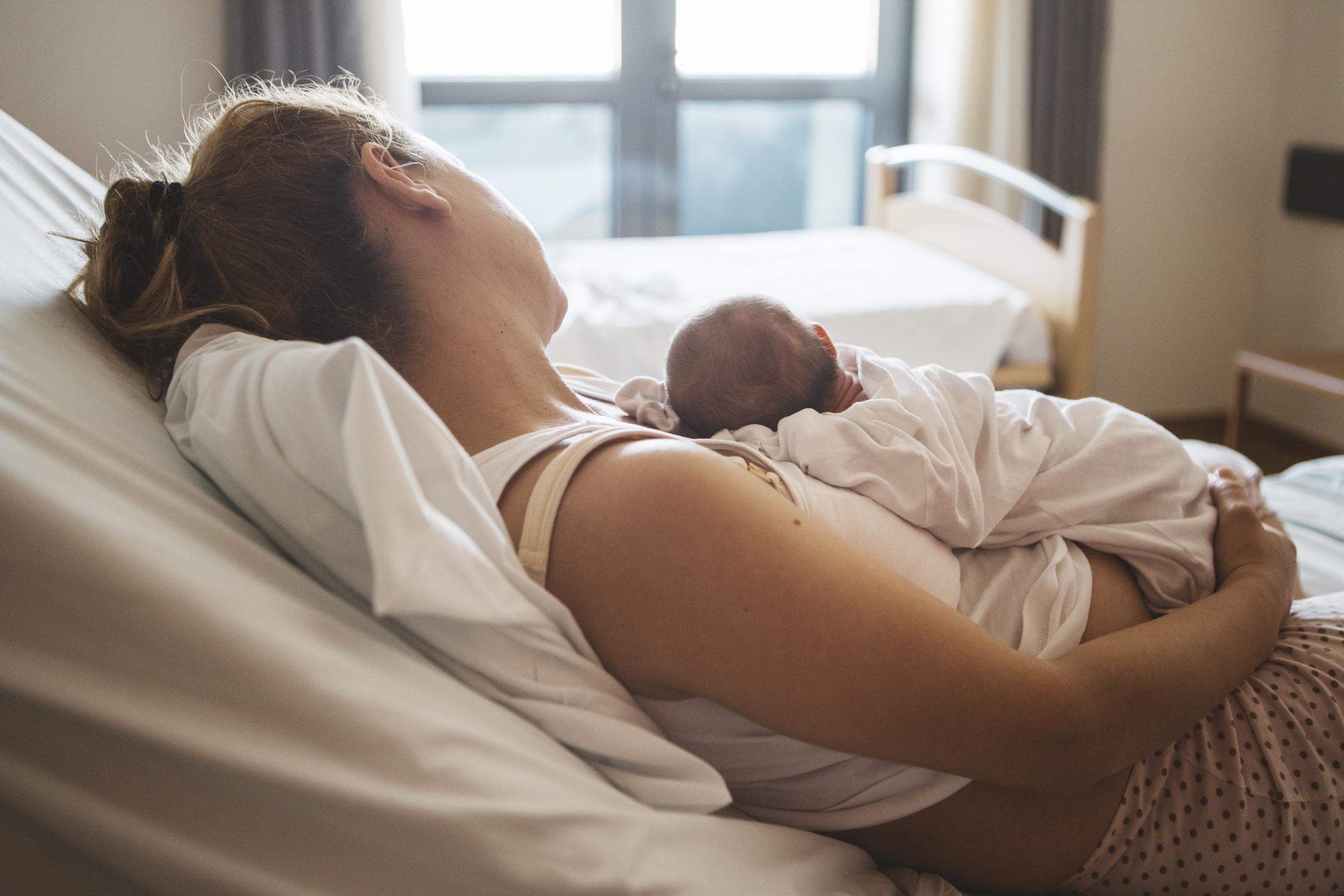 Une mère se repose dans un lit d'hôpital, tenant tendrement son nouveau-né dans ses bras I Photo d'illustration I Source : Getty Images