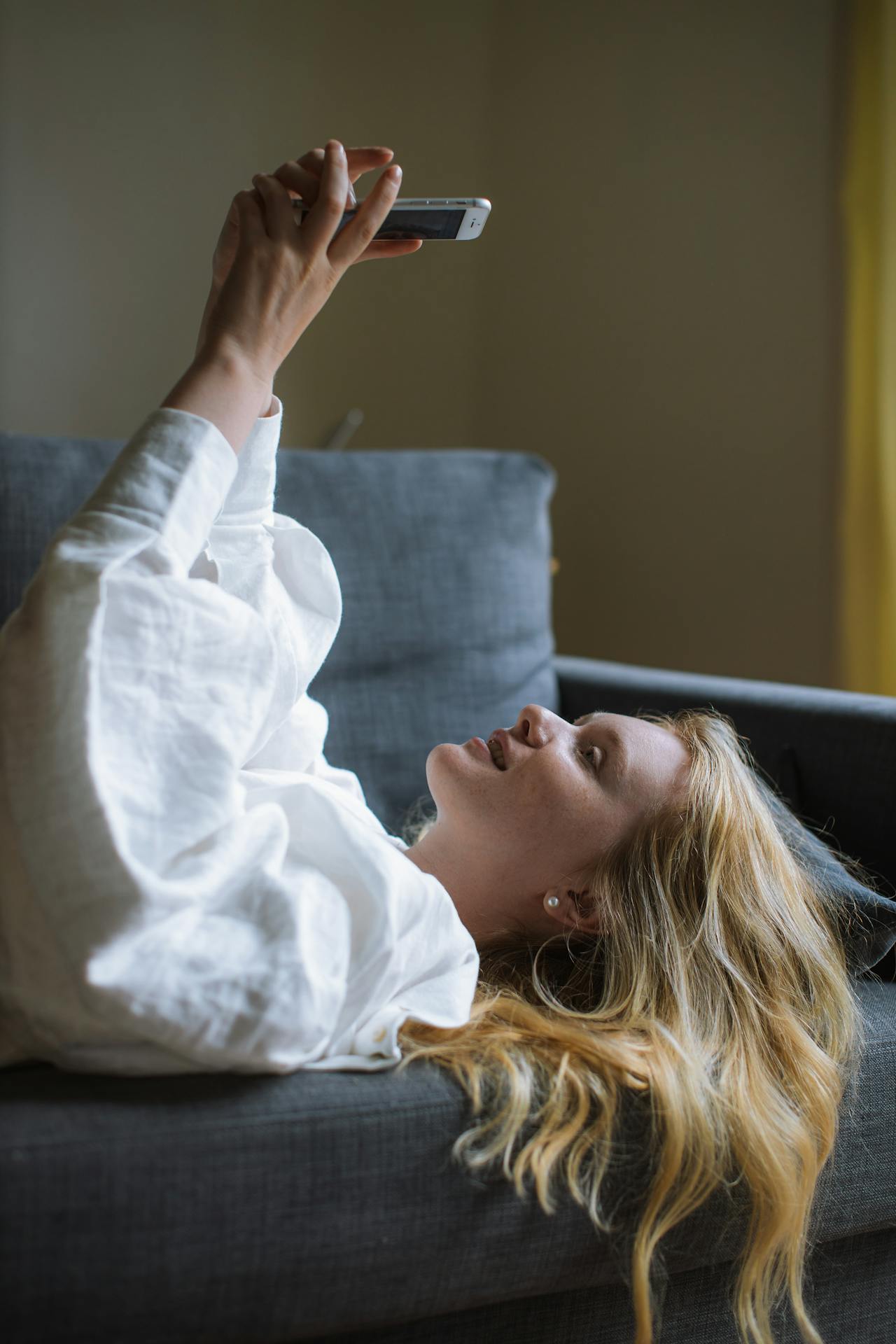 Une femme allongée sur le canapé et utilisant son téléphone | Source : Pexels