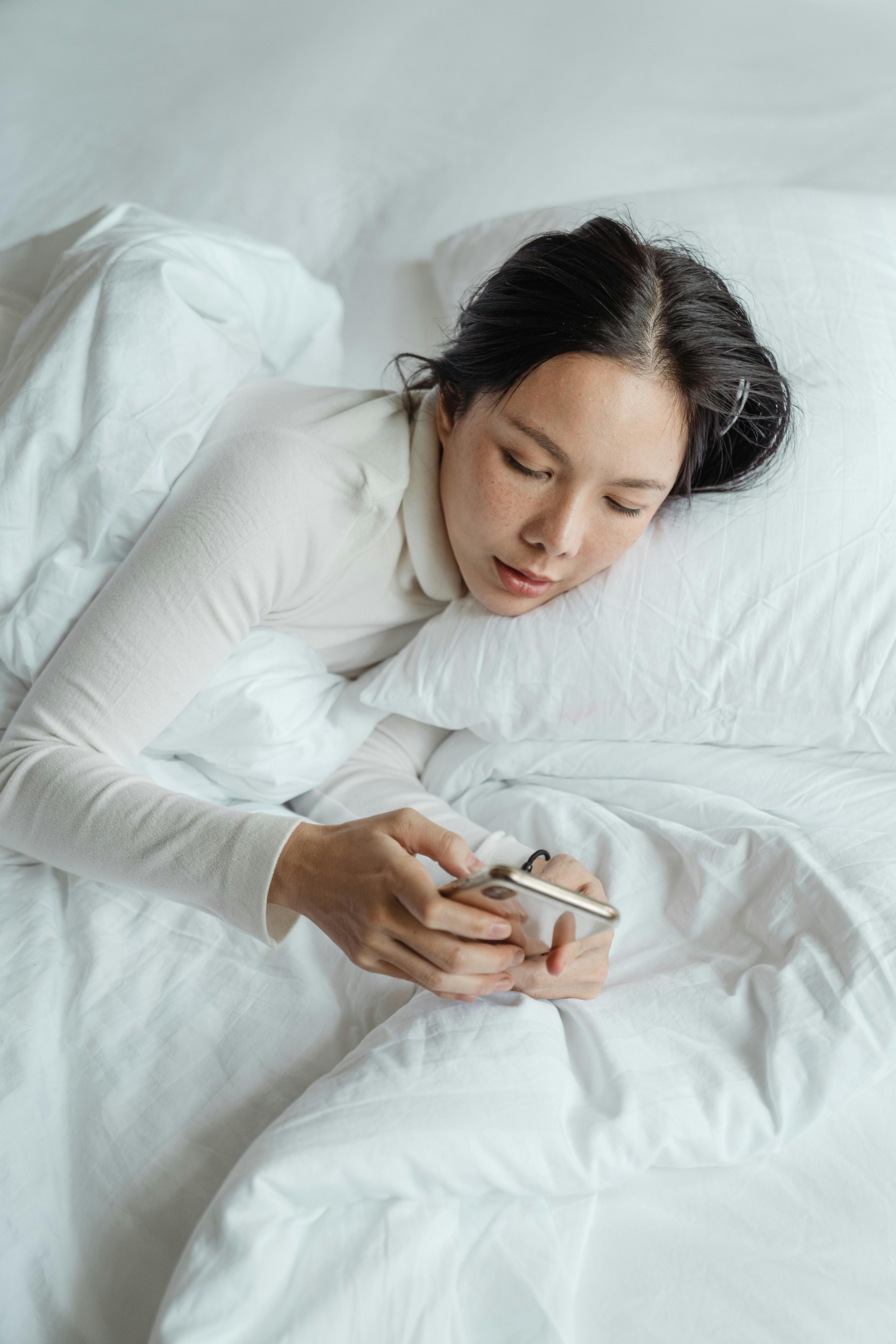 Une femme envoyant des textos sur son téléphone alors qu'elle est allongée dans son lit | Source : Pexels