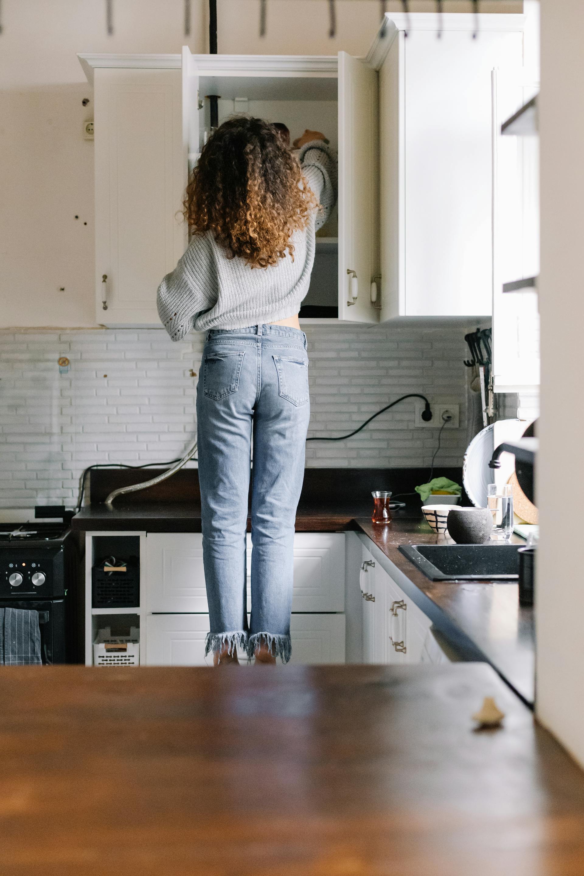 Vue arrière d'une femme ouvrant un meuble de cuisine | Source : Pexels