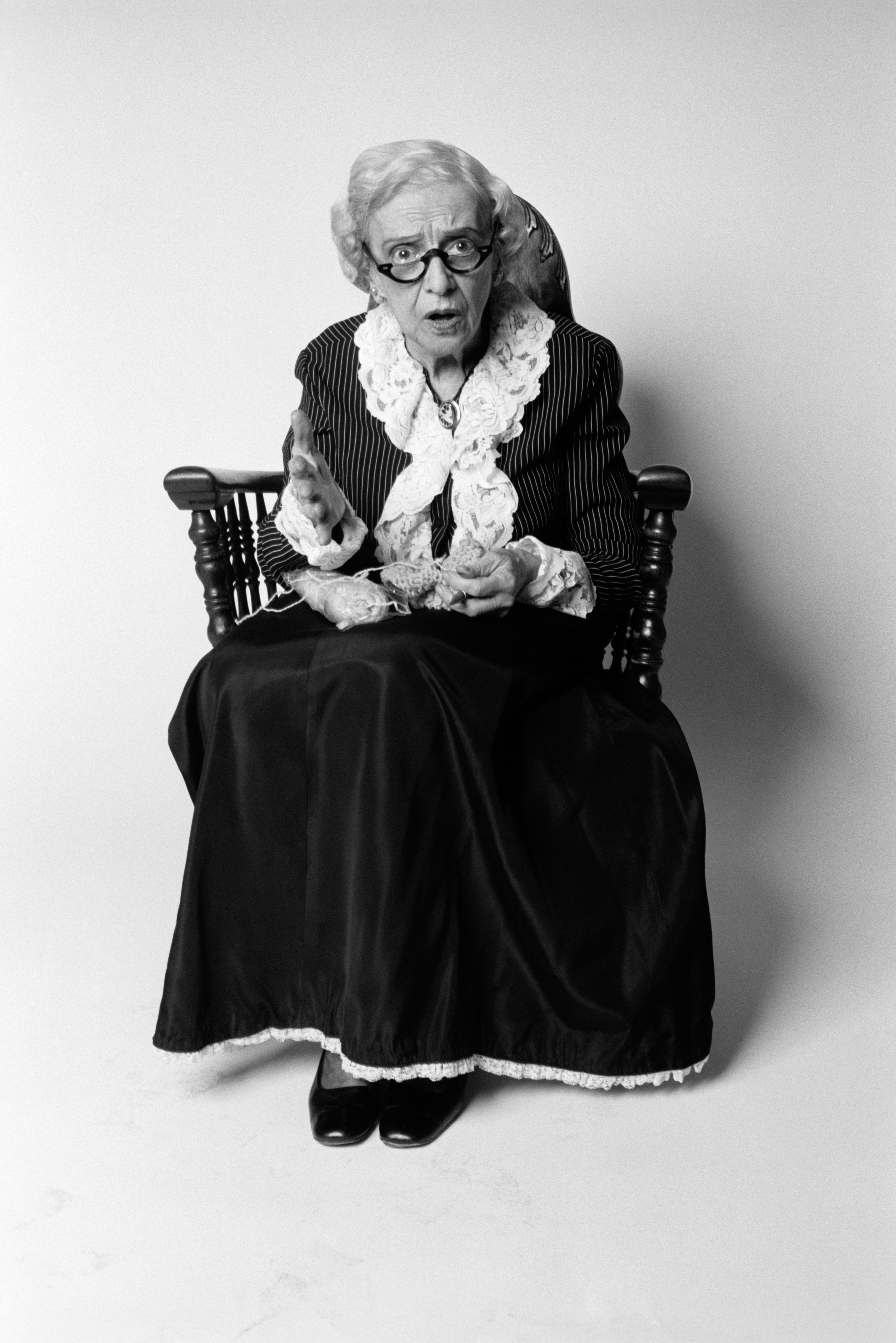 Une femme âgée choquée, assise sur une chaise avec un tricot sur les genoux | Source : Getty Images