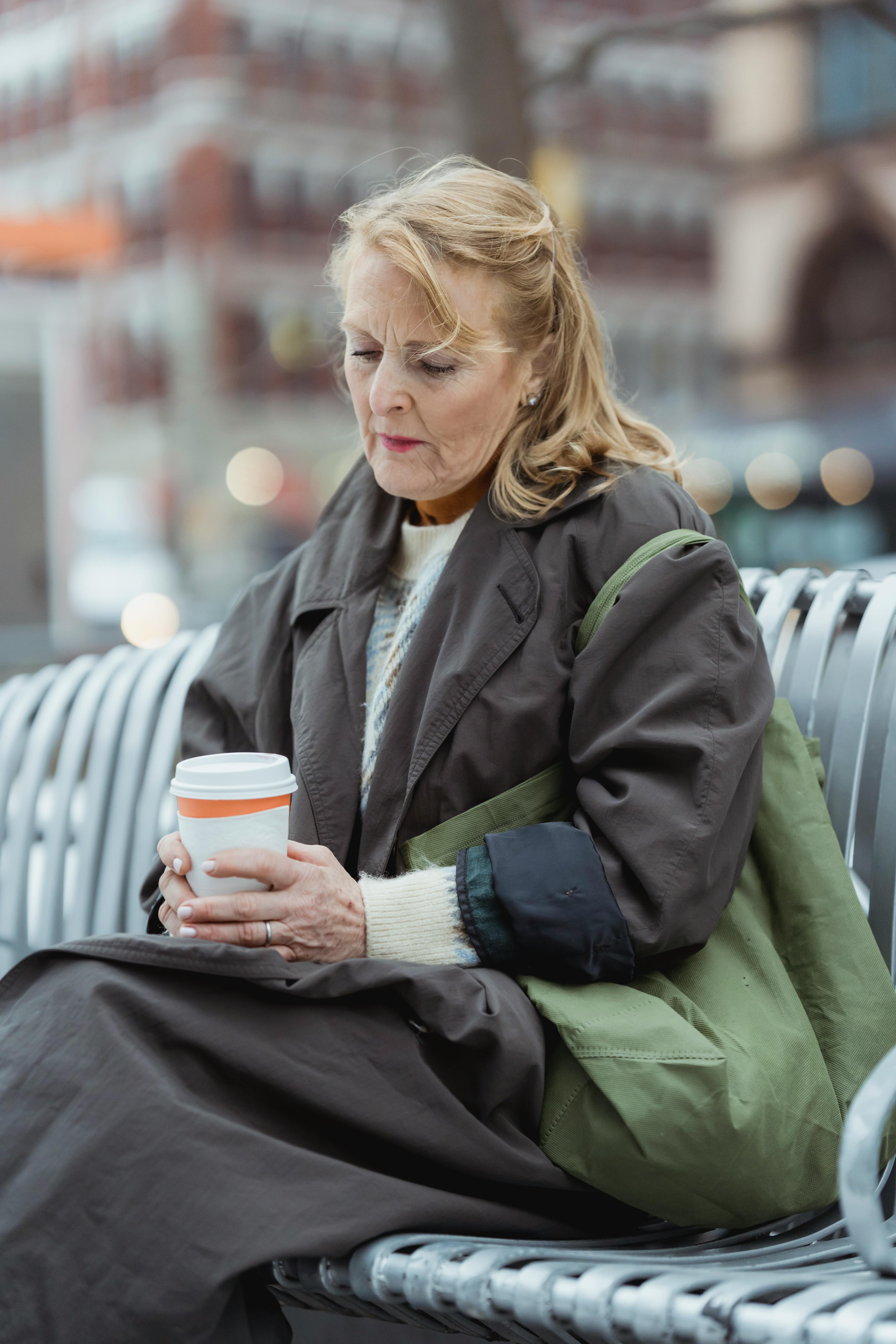 Une femme âgée contrariée tient une boisson alors qu'elle est assise sur un banc à l'extérieur | Source : Pexels