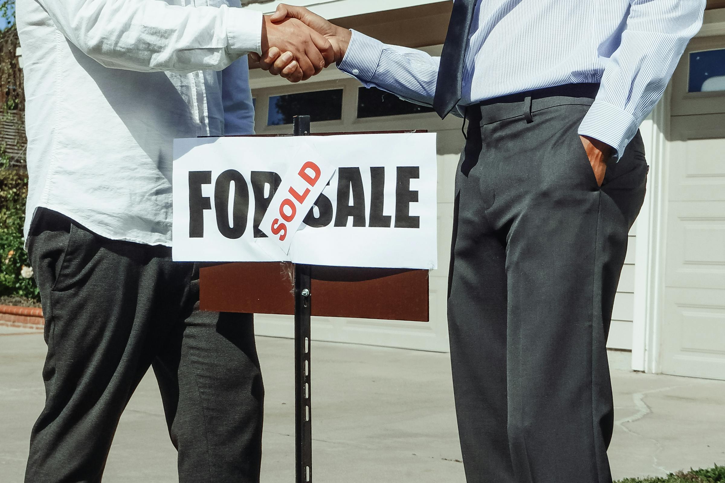 Two men shaking hands behind a "Sold" sign | Source: Pexels