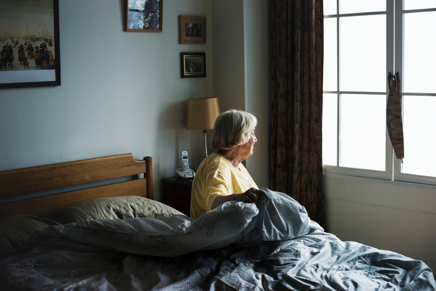 Une femme âgée solitaire assise sur son lit et regardant par la fenêtre | Source : Freepik