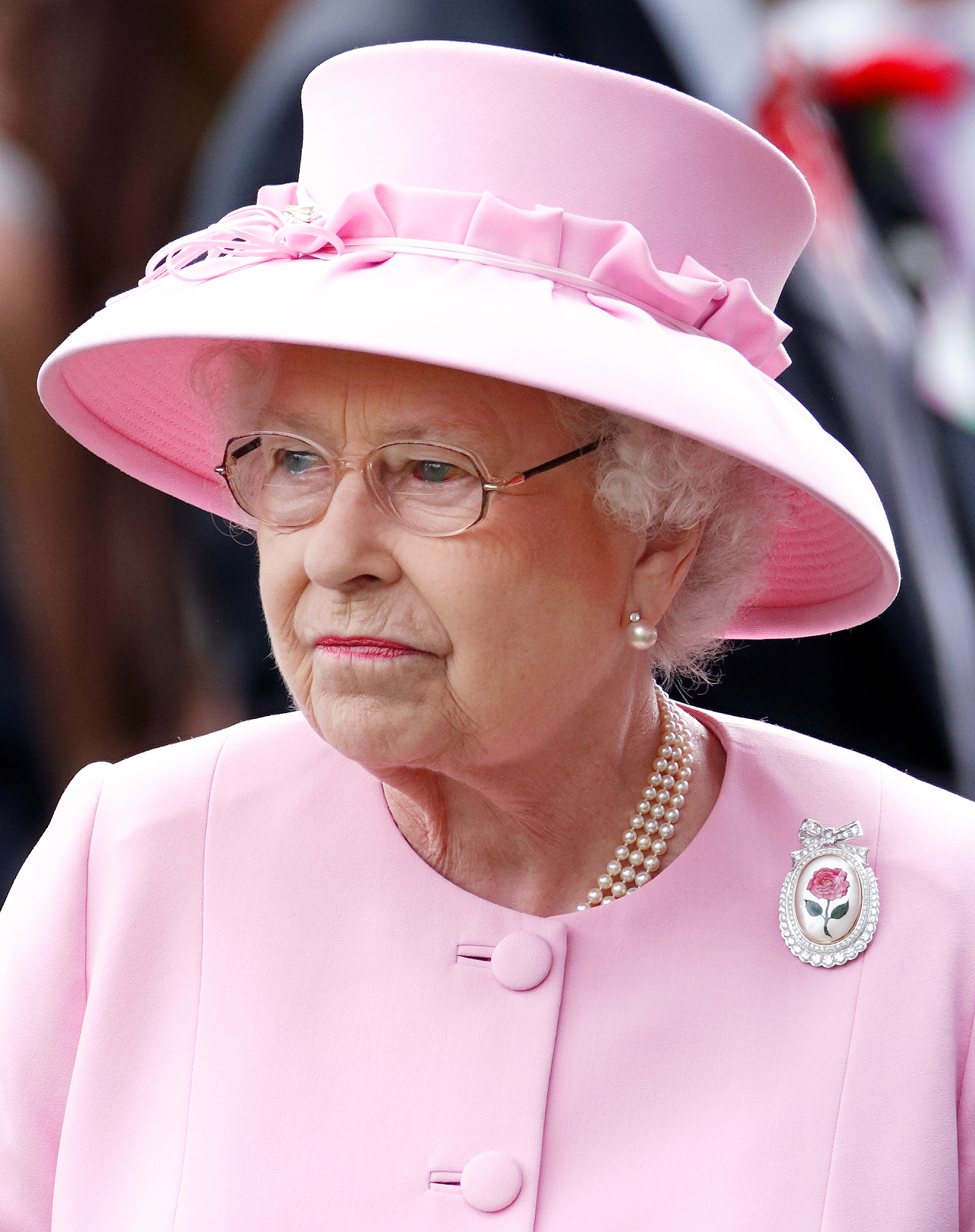 La reine Elizabeth II, qui présente une hémorragie dans l'œil gauche, porte la broche Centenary Rose lors de la deuxième journée du Royal Ascot 2012. Vêtue d'une tenue rose pastel et d'un chapeau assorti, la défunte monarque reste impassible lors de l'une de ses apparitions à cet événement prestigieux.
