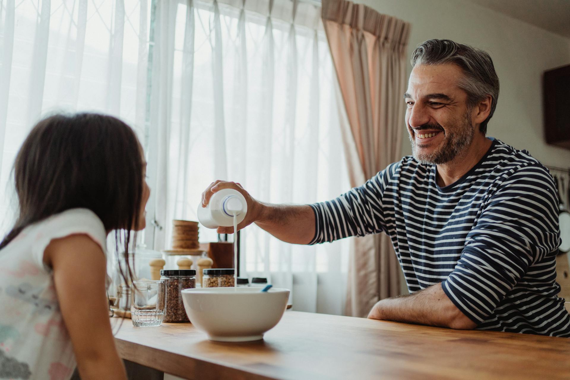 Un homme qui verse du lait dans un bol pendant que sa fille le regarde | Source : Pexels