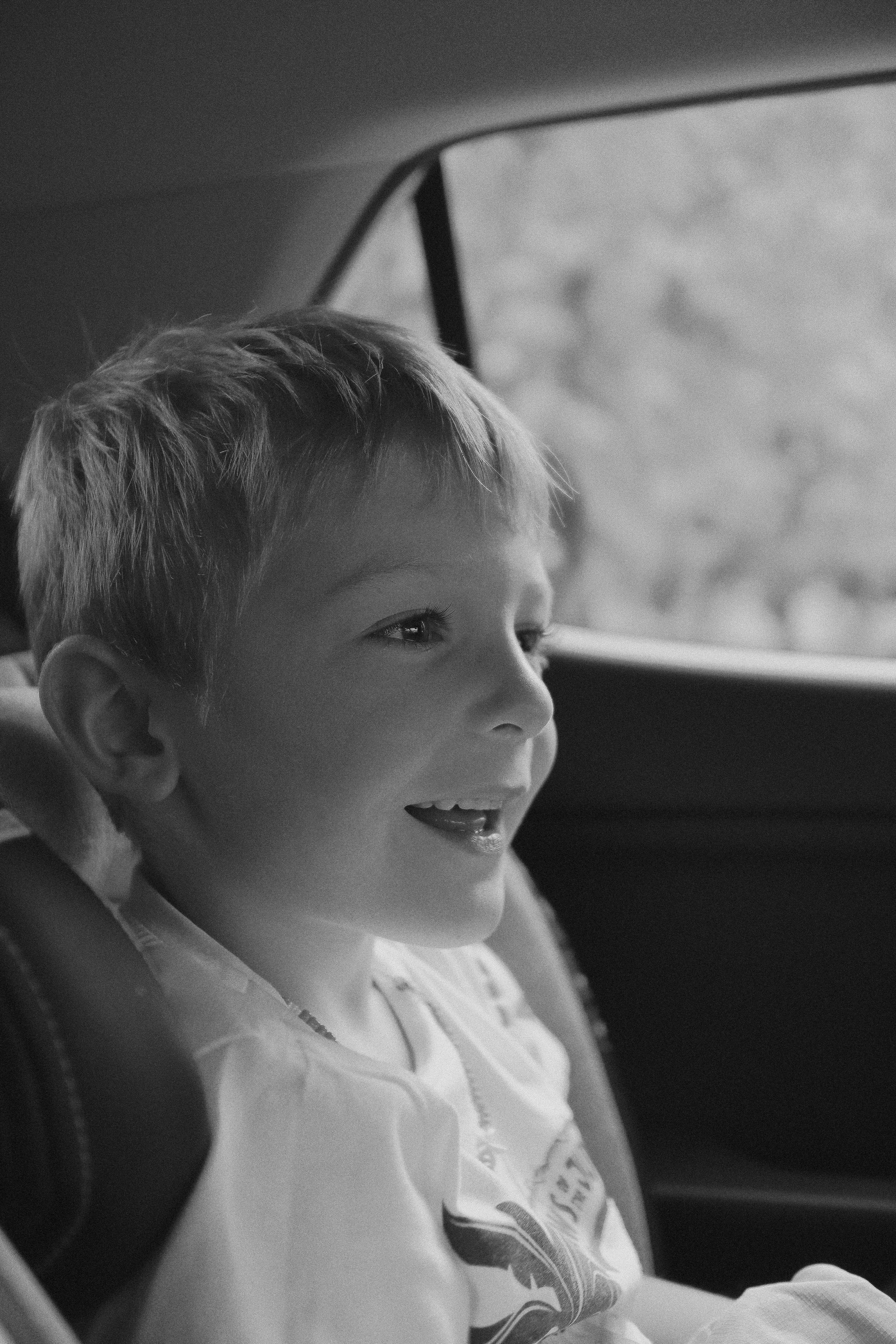 Photo en niveaux de gris d'un jeune garçon assis sur la banquette arrière d'une voiture | Source : Unsplash