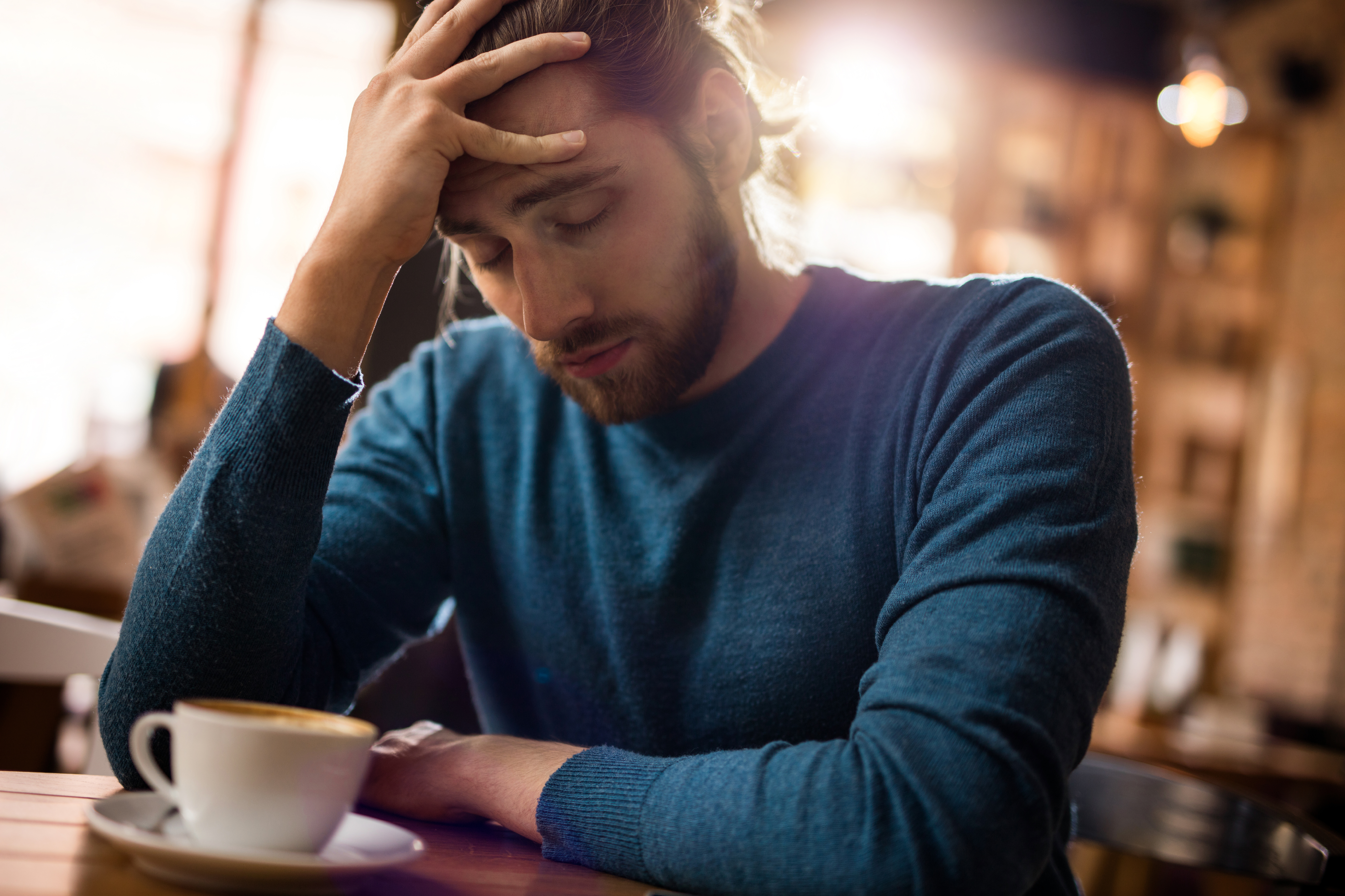 Homme stressé se tenant la tête de douleur dans un café | Source : Getty Images