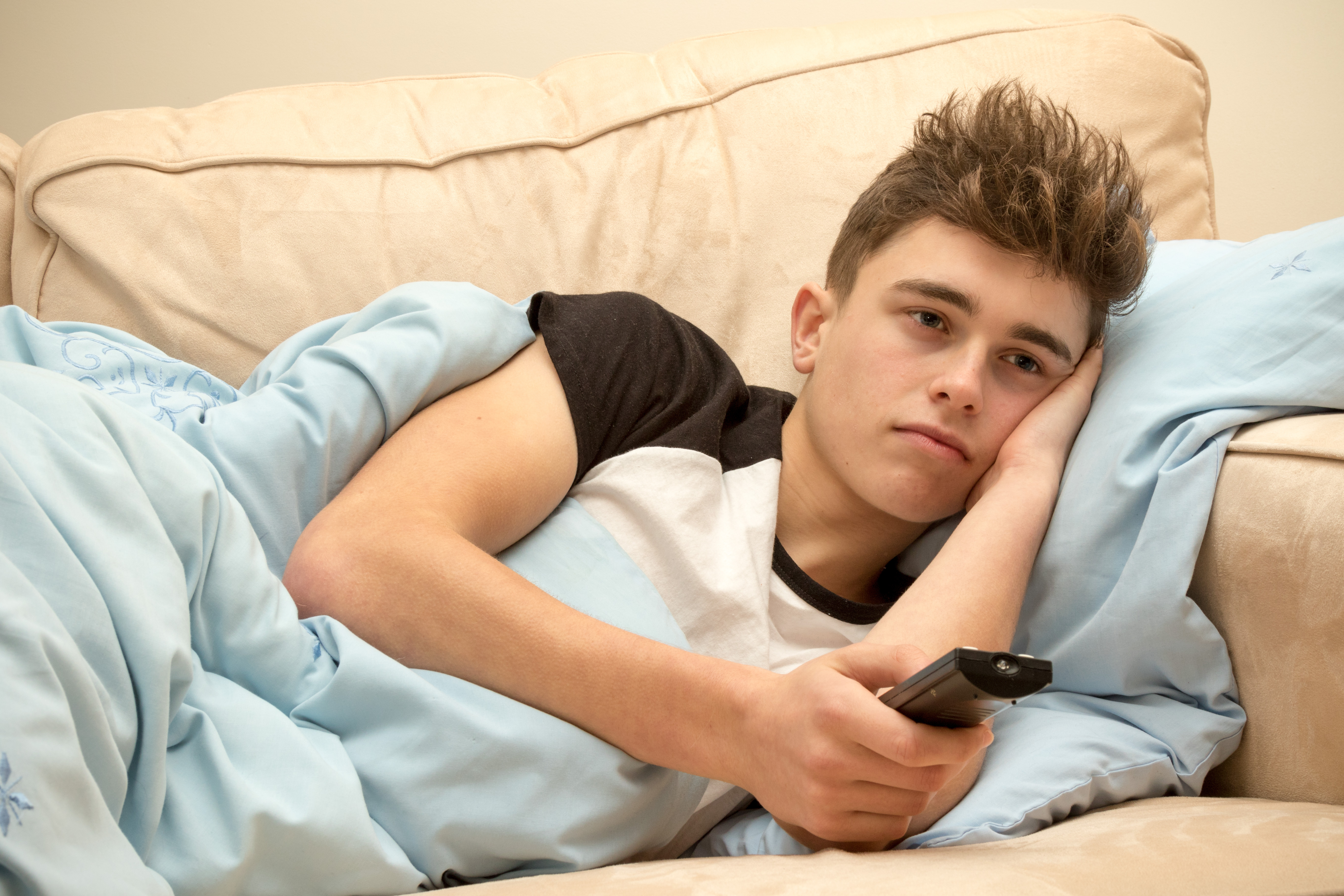 Un jeune homme paresseux regardant la télévision sur un canapé | Source : Shutterstock